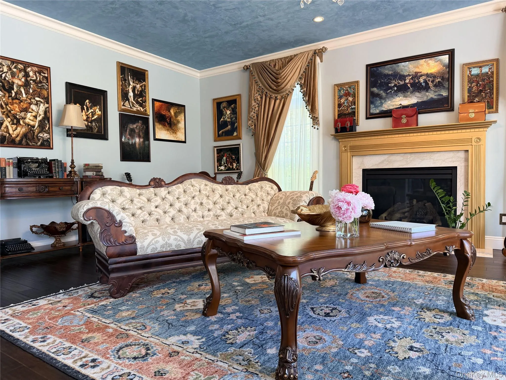 Living area featuring a detailed fireplace with a gold-finished mantel, a light blue wall color, and crown molding Living area featuring a detailed fireplace with a gold-finished mantel, a light blue wall color, and crown molding