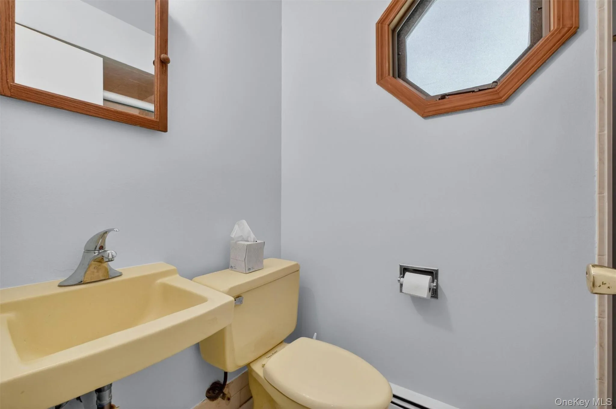 1st Fl. Full Bath featuring a wall-mounted sink, toilet, and an octagonal window with wood trim 1st Fl. Full Bath featuring a wall-mounted sink, toilet, and an octagonal window with wood trim