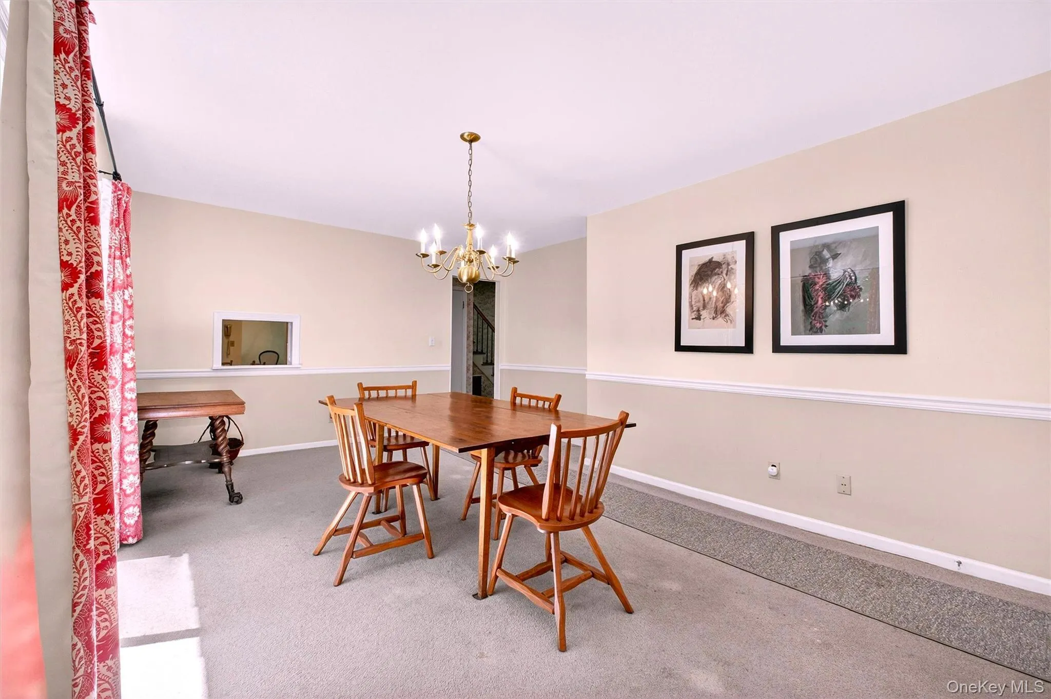 Formal dining room featuring a brass chandelier, two-tone painted walls with chair rail molding, and a pass-through window Formal dining room featuring a brass chandelier, two-tone painted walls with chair rail molding, and a pass-through window