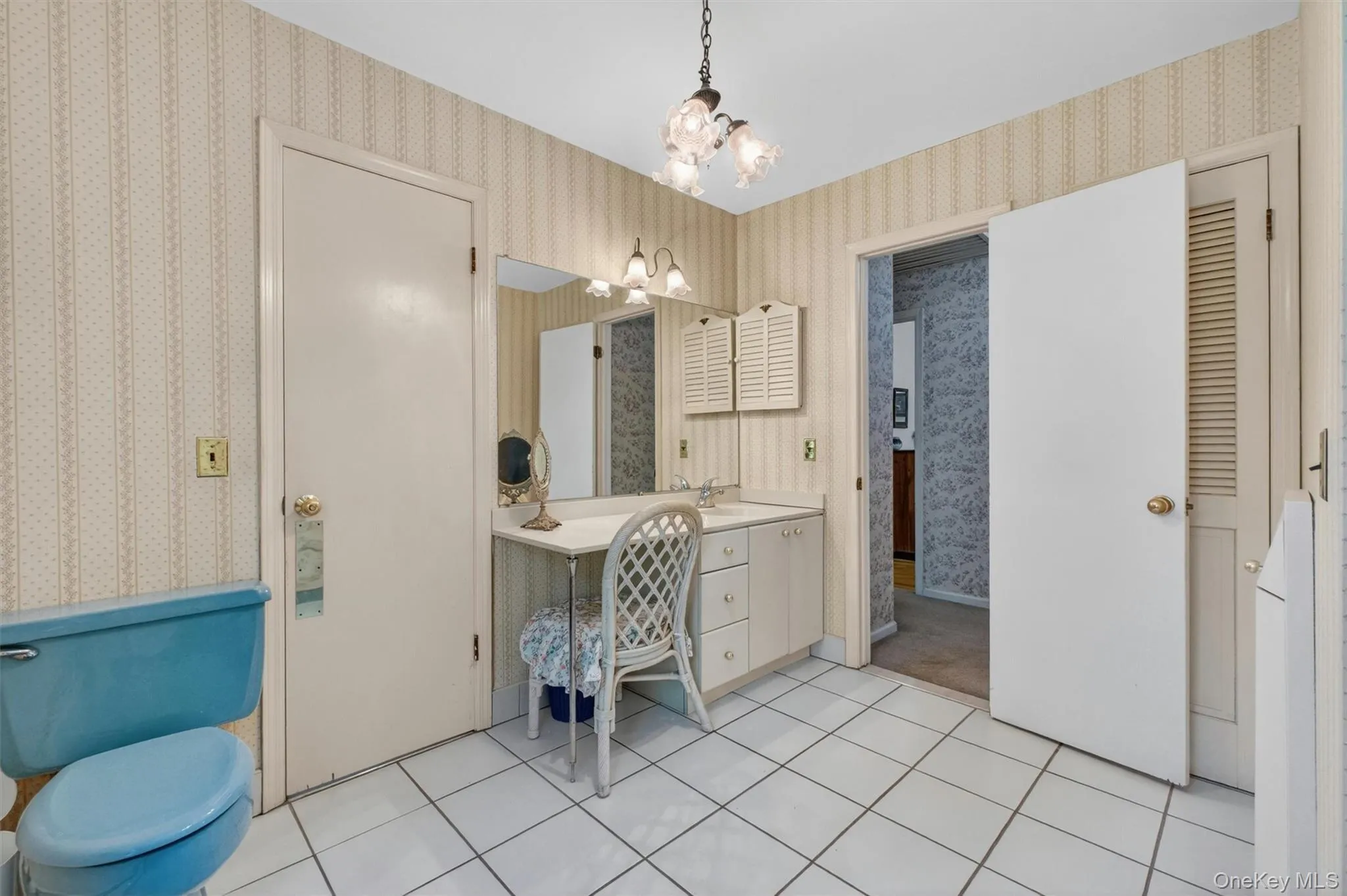 Bathroom with white ceramic tile flooring, a single vanity with storage, a makeup vanity, and two paneled doors Bathroom with white ceramic tile flooring, a single vanity with storage, a makeup vanity, and two paneled doors