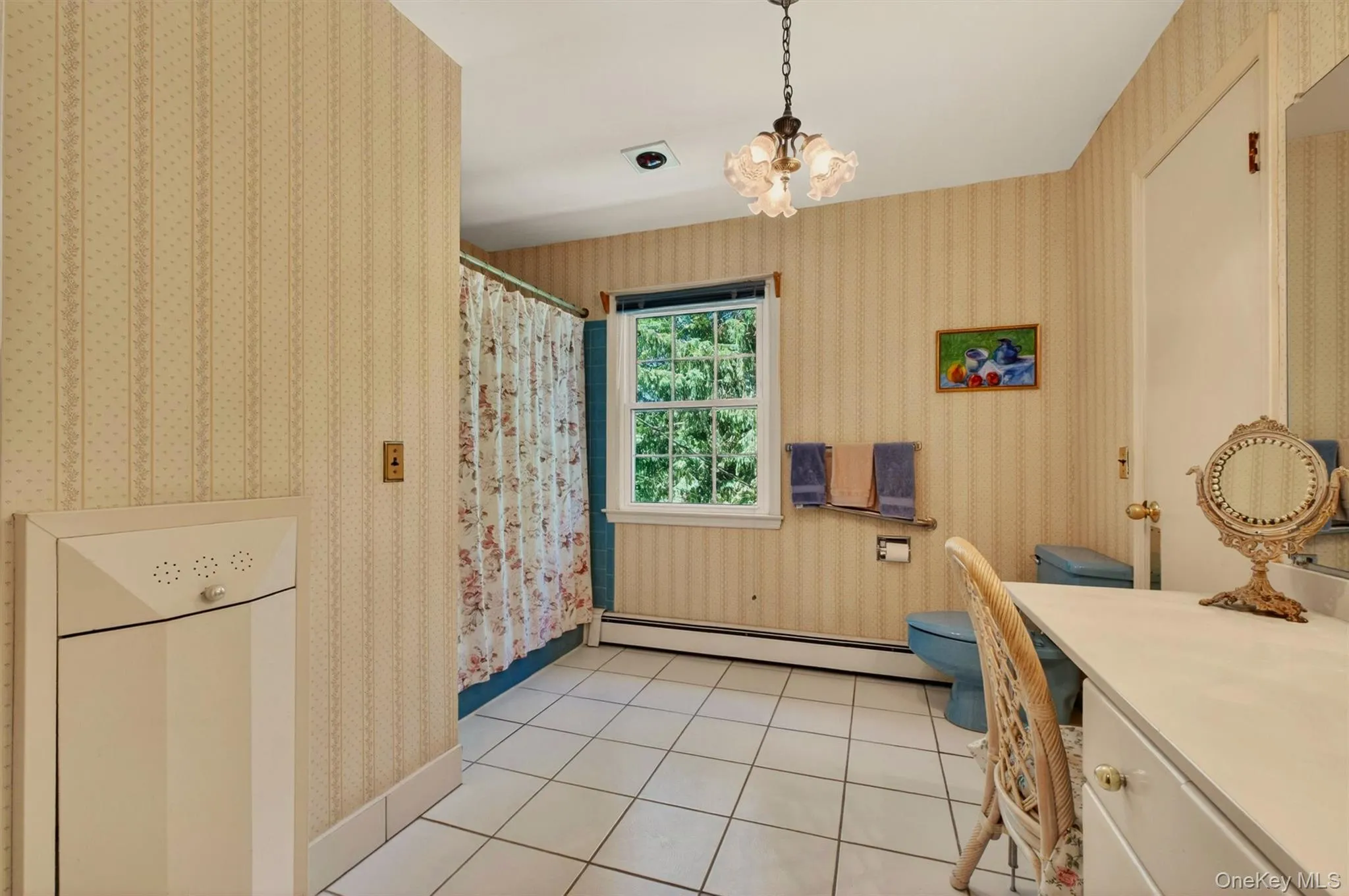 Bathroom featuring a vanity desk, white tile flooring, patterned wallpaper, a window, and a light fixture Bathroom featuring a vanity desk, white tile flooring, patterned wallpaper, a window, and a light fixture