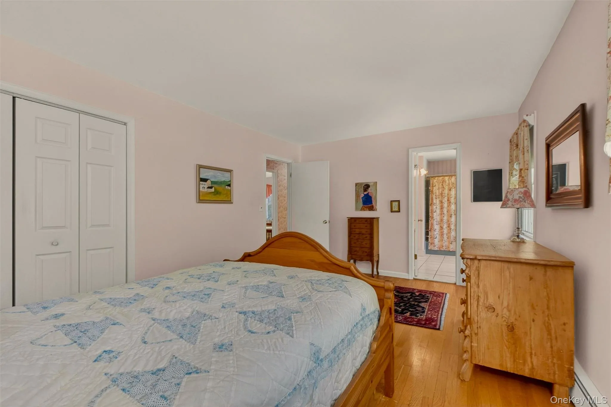 Primary bedroom w/hardwood flooring & access to dual entry full bath, complemented by light-toned wall paint and white trim work Primary bedroom w/hardwood flooring & access to dual entry full bath, complemented by light-toned wall paint and white trim work