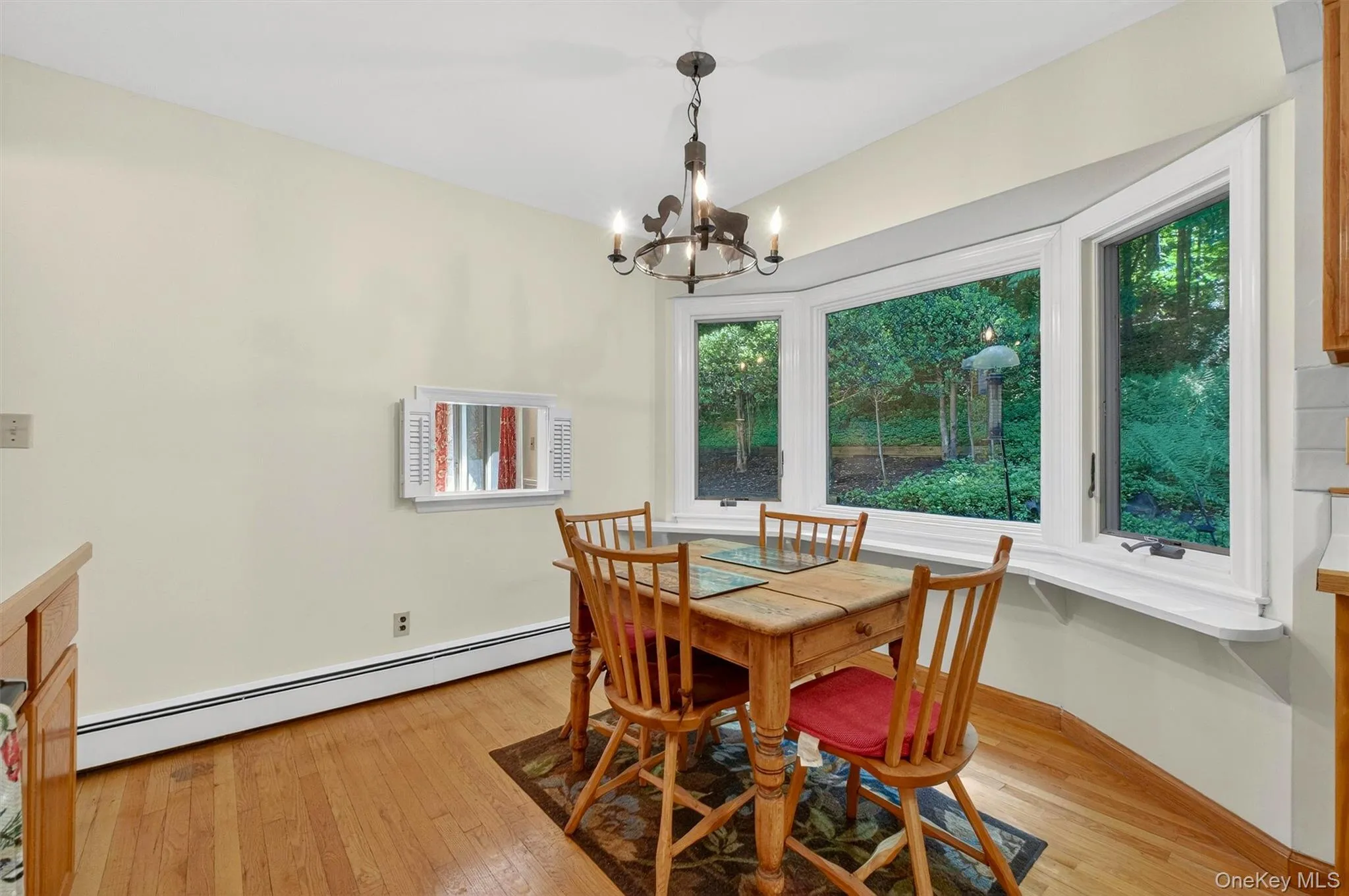 Bay window with exterior landscaping, wood-finish flooring, cream-toned walls, and a built-in kitchen counter with wood cabinetry Bay window with exterior landscaping, wood-finish flooring, cream-toned walls, and a built-in kitchen counter with wood cabinetry