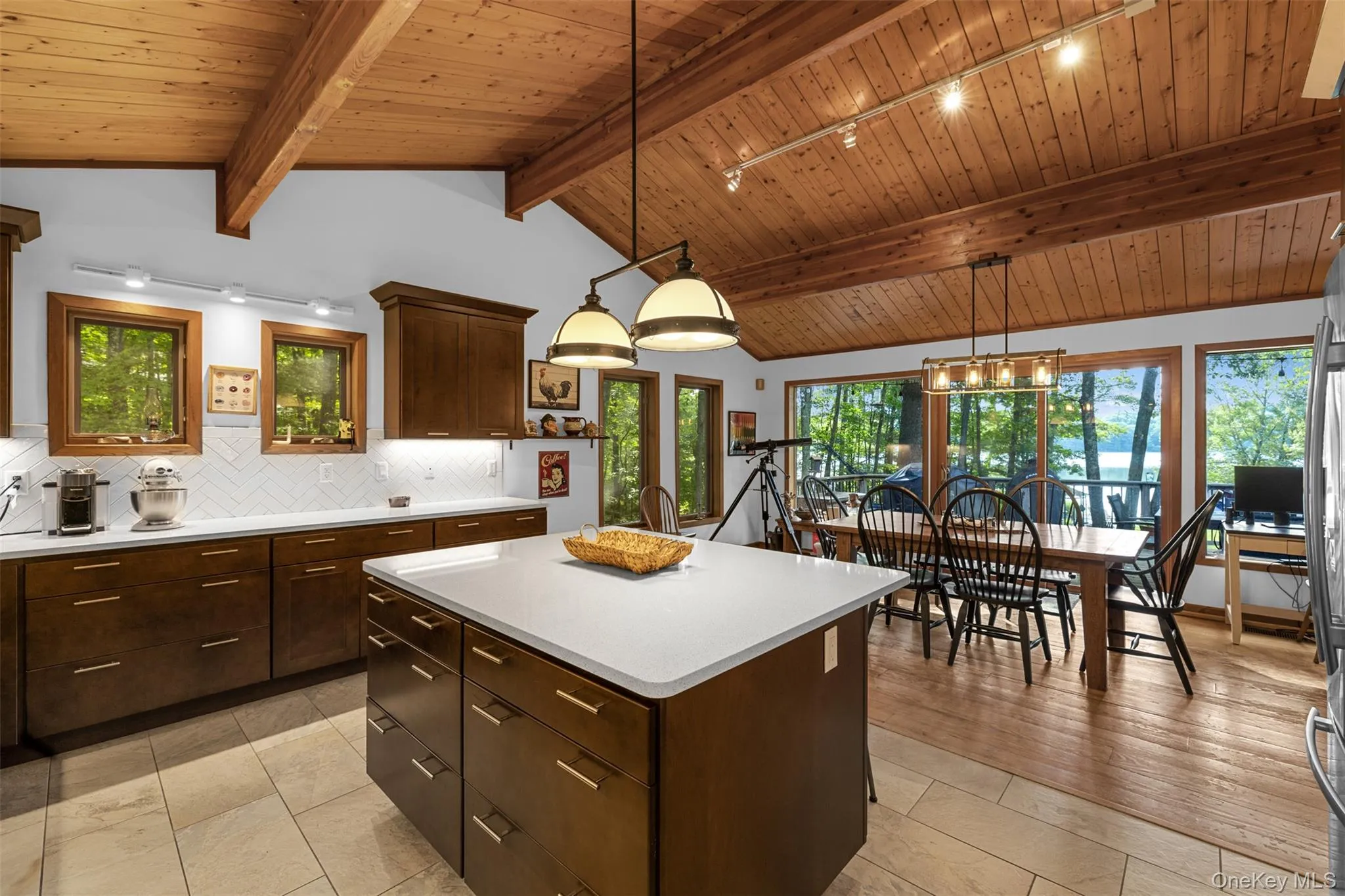 Kitchen with rail lighting, wooden ceiling, light countertops, tasteful backsplash, and a center island Kitchen with rail lighting, wooden ceiling, light countertops, tasteful backsplash, and a center island