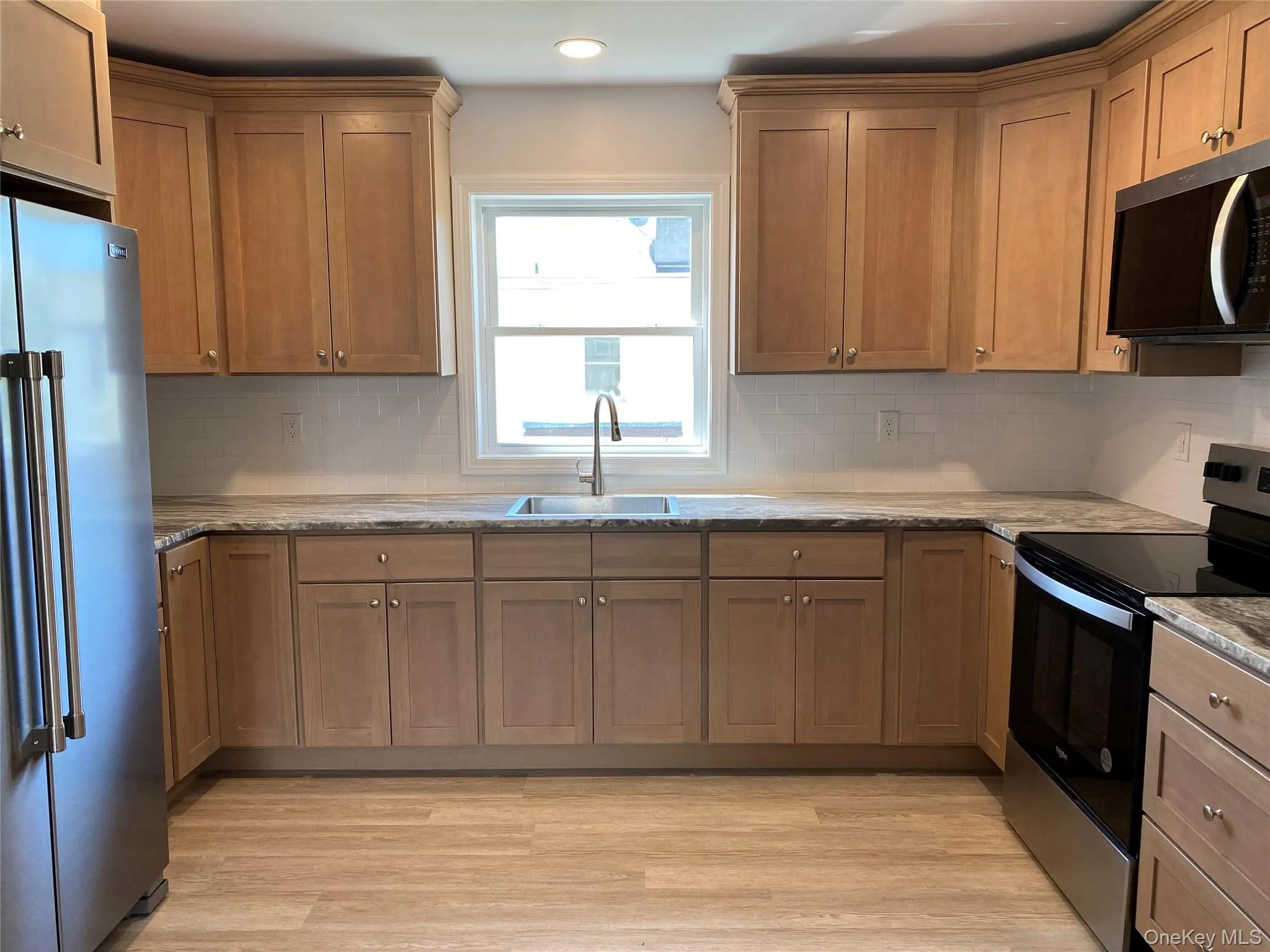 Kitchen featuring stainless steel appliances, decorative backsplash, light wood finished floors, brown cabinets, and recessed lighting Kitchen featuring stainless steel appliances, decorative backsplash, light wood finished floors, brown cabinets, and recessed lighting