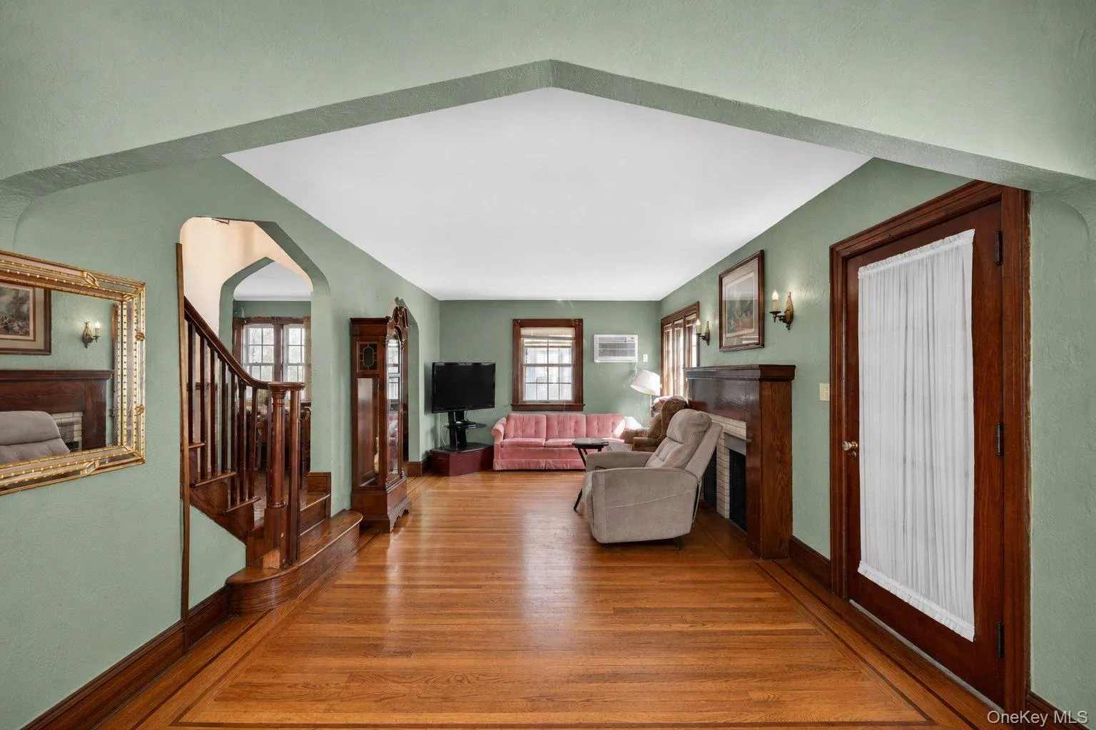 Hardwood flooring with a decorative border, featuring a staircase with wood railing and an arched entryway Hardwood flooring with a decorative border, featuring a staircase with wood railing and an arched entryway
