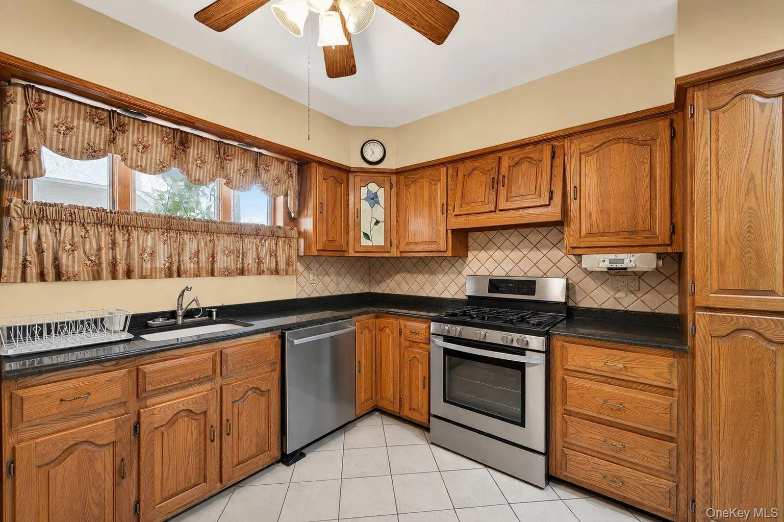 Kitchen featuring solid wood cabinetry, black countertops, a stainless steel range, stainless steel dishwasher, and a white tile floor Kitchen featuring solid wood cabinetry, black countertops, a stainless steel range, stainless steel dishwasher, and a white tile floor