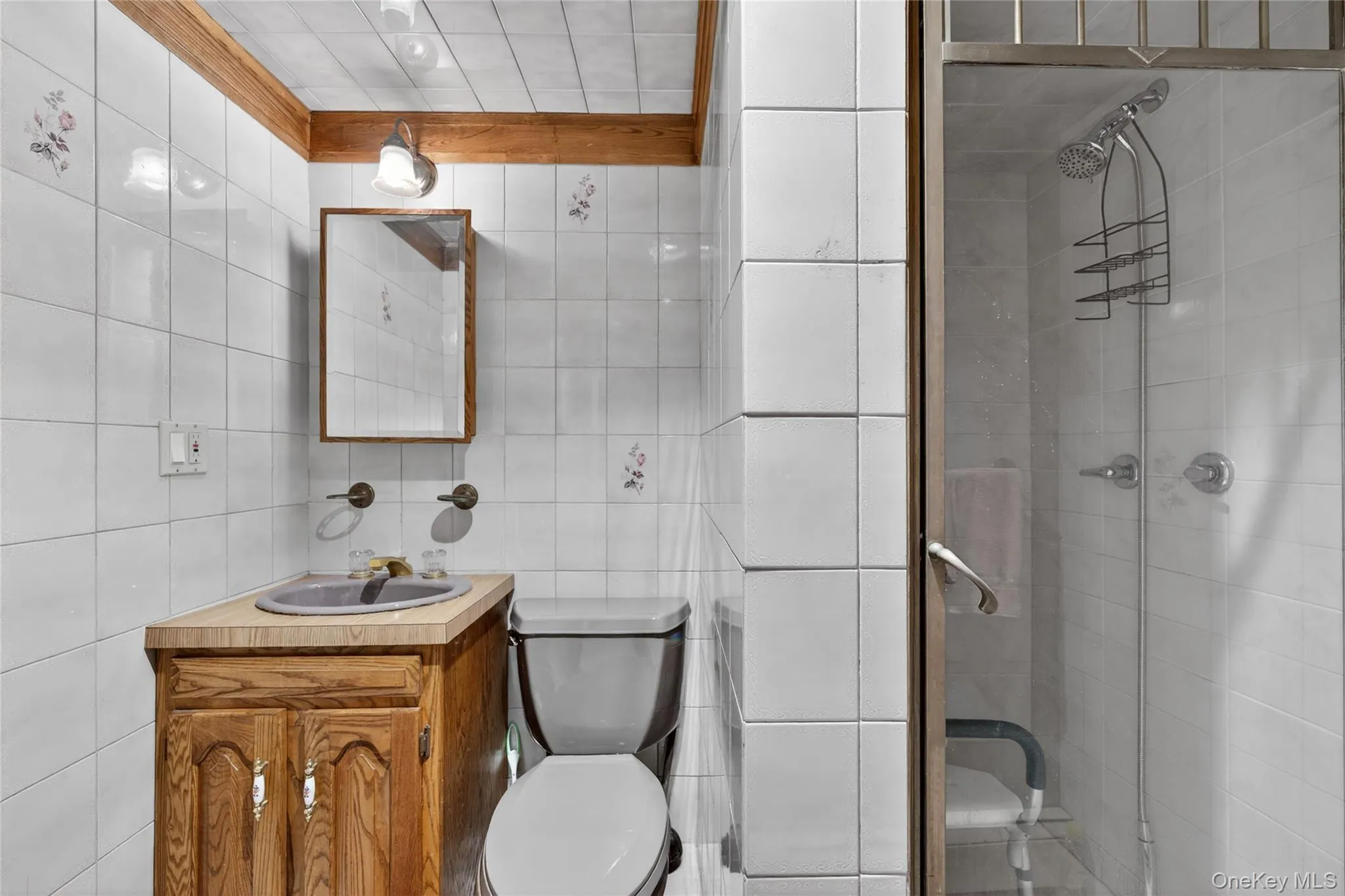 Bathroom featuring white tile walls, a wood vanity with a gray sink, a mirrored medicine cabinet, and a glass-enclosed shower with a chrome showerhead Bathroom featuring white tile walls, a wood vanity with a gray sink, a mirrored medicine cabinet, and a glass-enclosed shower with a chrome showerhead