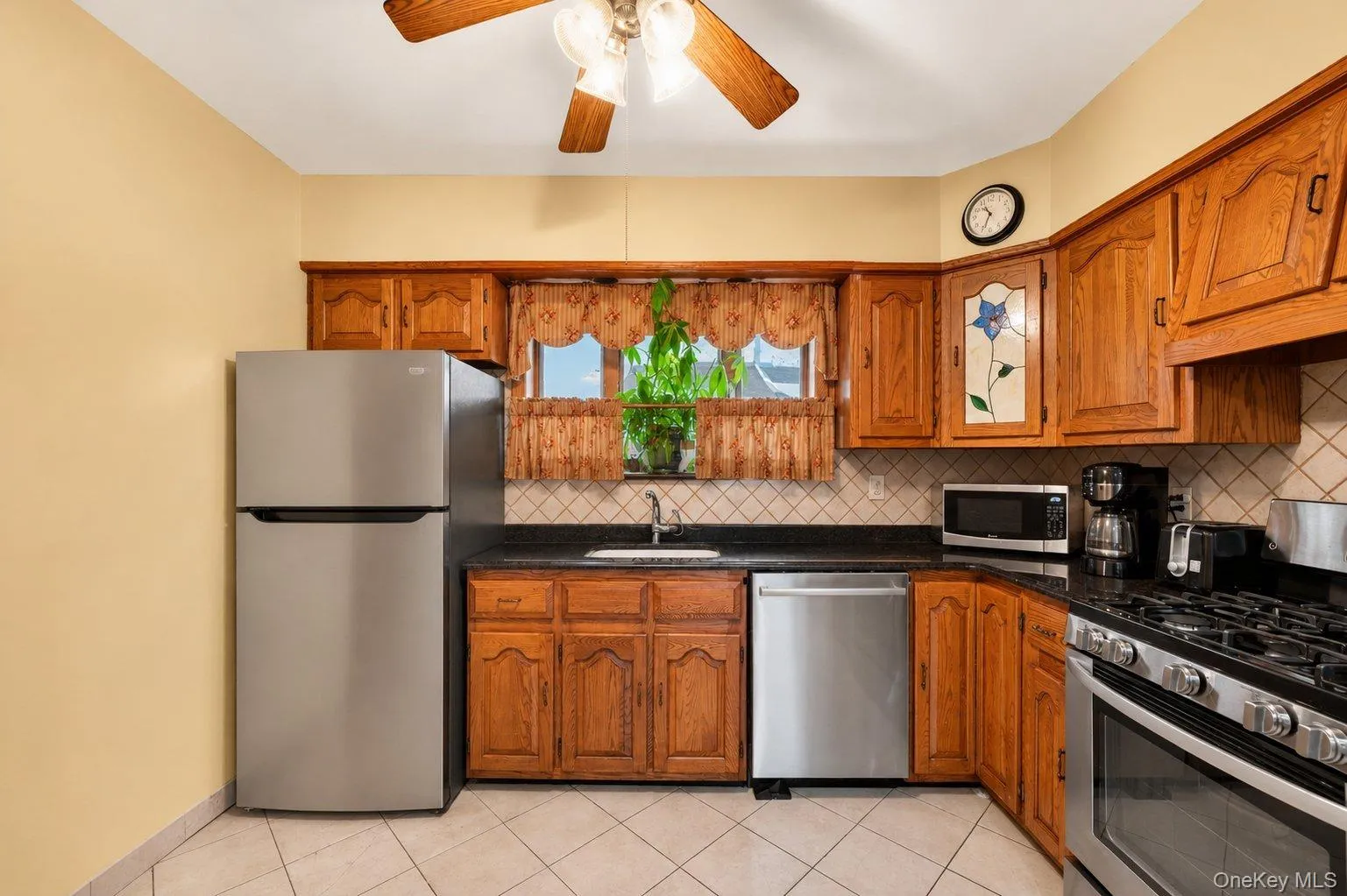Kitchen featuring wood cabinetry, stainless steel appliances, dark countertops, and a tiled backsplash Kitchen featuring wood cabinetry, stainless steel appliances, dark countertops, and a tiled backsplash