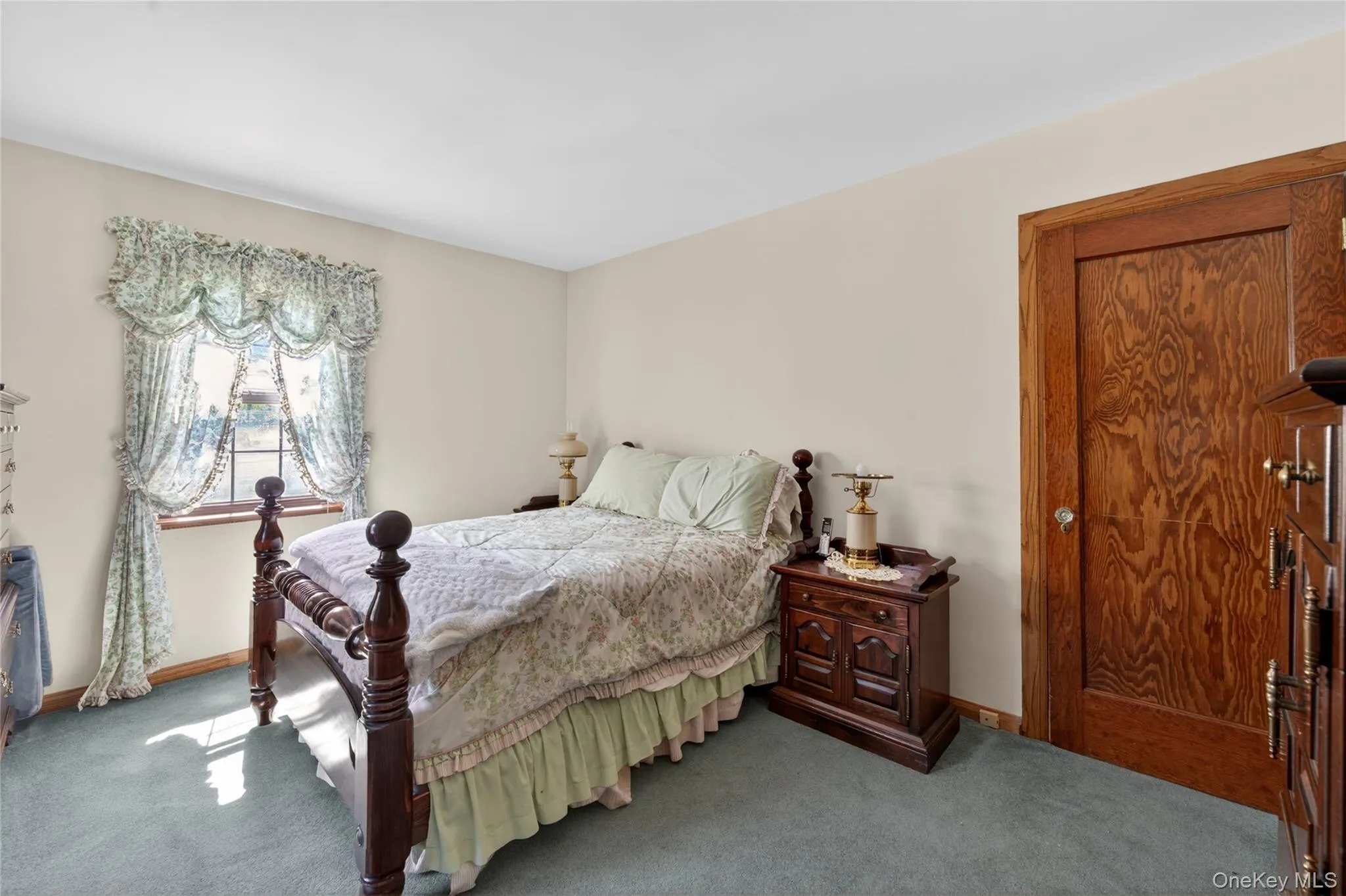 Bedroom featuring a window with natural light, light-toned walls, and a wood-finish door with matching trim Bedroom featuring a window with natural light, light-toned walls, and a wood-finish door with matching trim