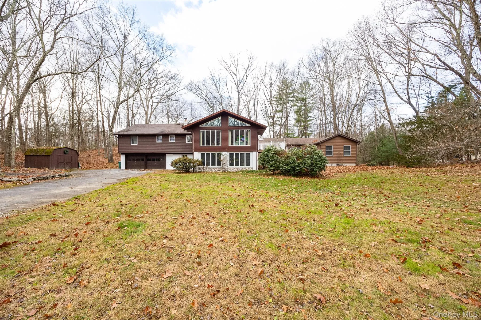 Split level home featuring driveway, an attached garage, a front lawn, and view of wooded area Split level home featuring driveway, an attached garage, a front lawn, and view of wooded area