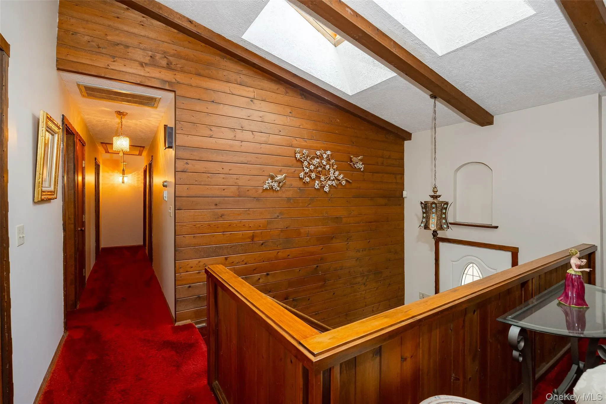 Corridor with vaulted ceiling, dark colored carpet, a skylight, wood walls, and a textured ceiling Corridor with vaulted ceiling, dark colored carpet, a skylight, wood walls, and a textured ceiling