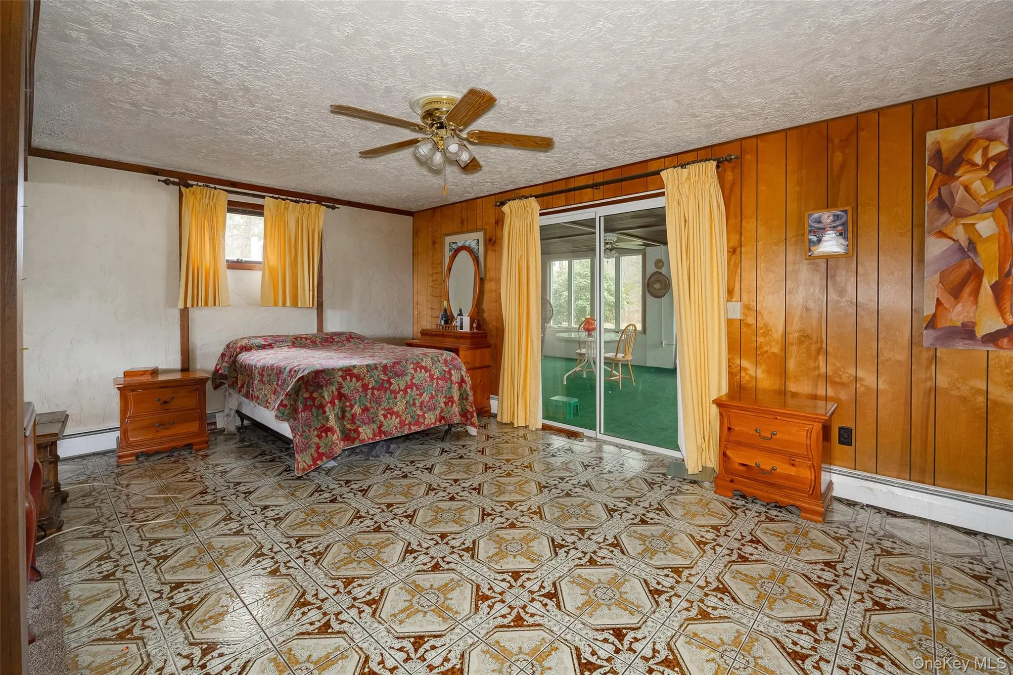 Bedroom with ceiling fan, baseboard heating, light floors, wooden walls, and a textured ceiling Bedroom with ceiling fan, baseboard heating, light floors, wooden walls, and a textured ceiling