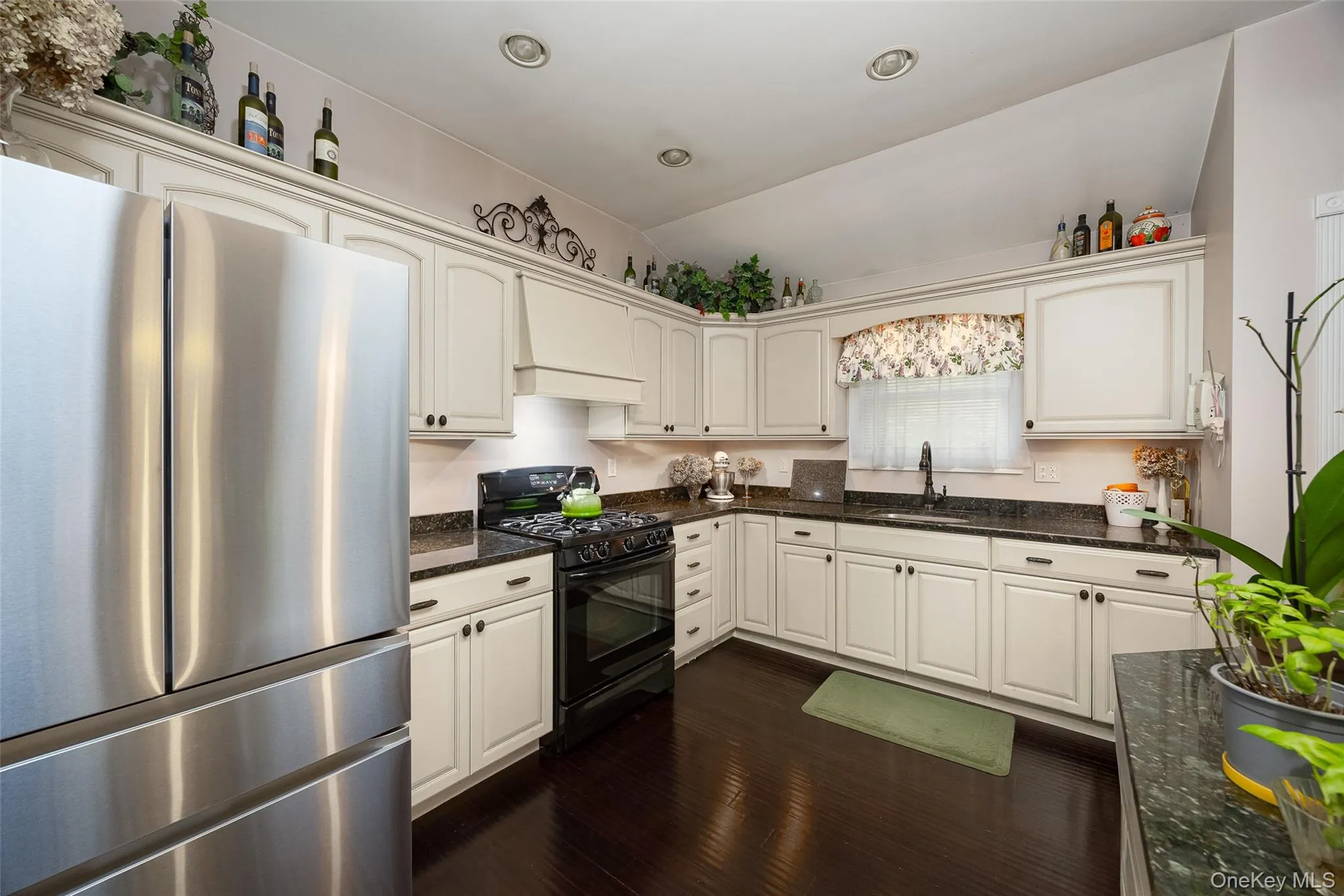Kitchen featuring freestanding refrigerator, black range with gas cooktop, custom range hood, dark stone countertops, and dark wood-style floors Kitchen featuring freestanding refrigerator, black range with gas cooktop, custom range hood, dark stone countertops, and dark wood-style floors