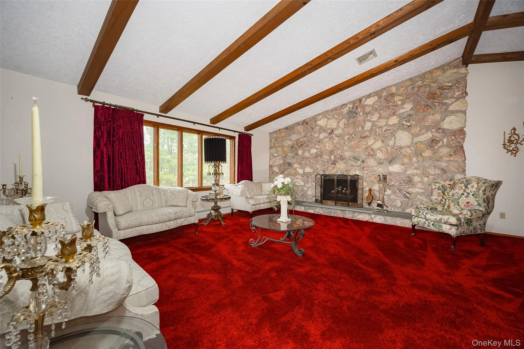 Living room with carpet, a stone fireplace, and a baseboard heating unit Living room with carpet, a stone fireplace, and a baseboard heating unit