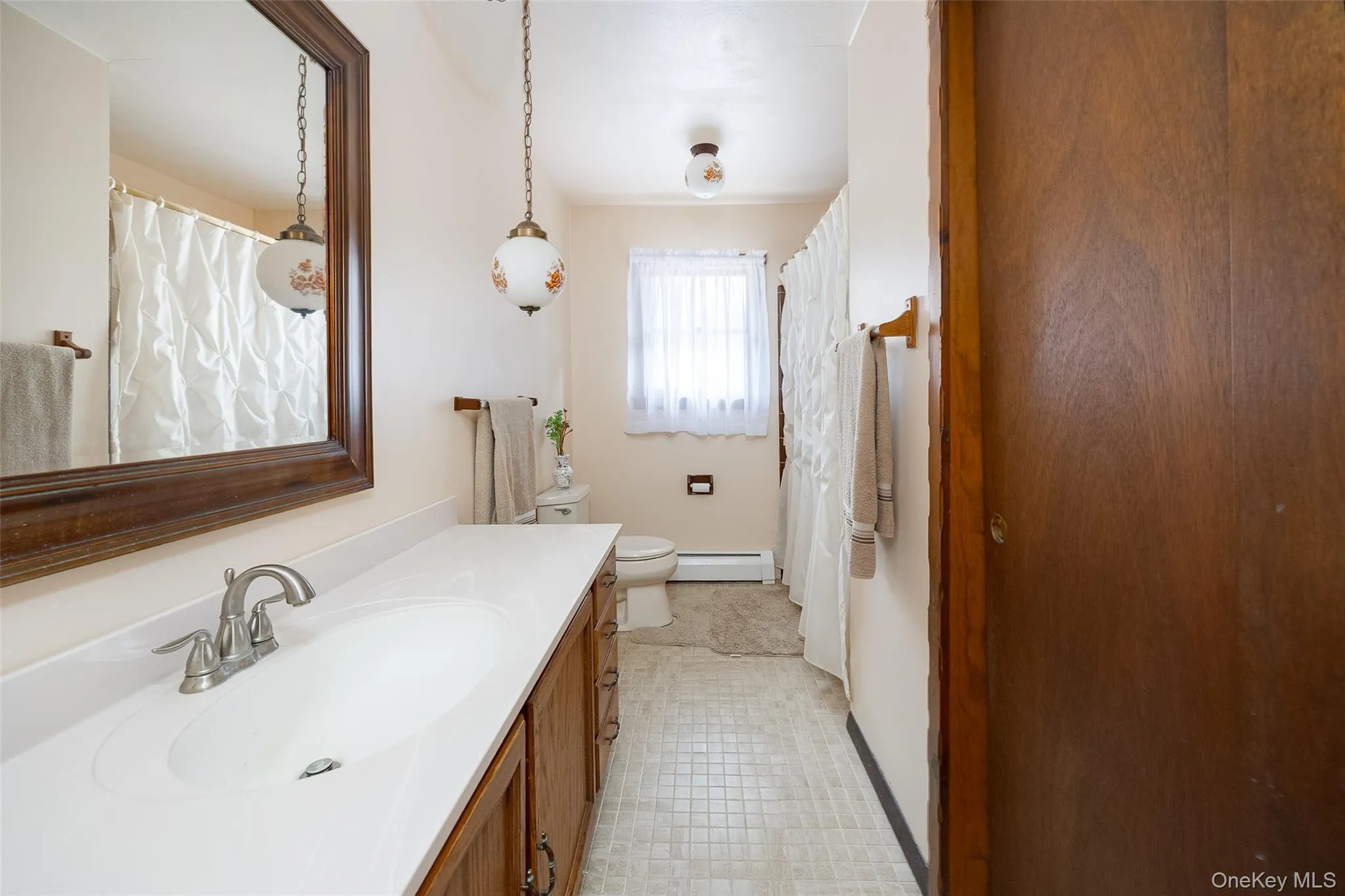 Full bathroom featuring curtained shower, vanity, and a baseboard heating unit Full bathroom featuring curtained shower, vanity, and a baseboard heating unit