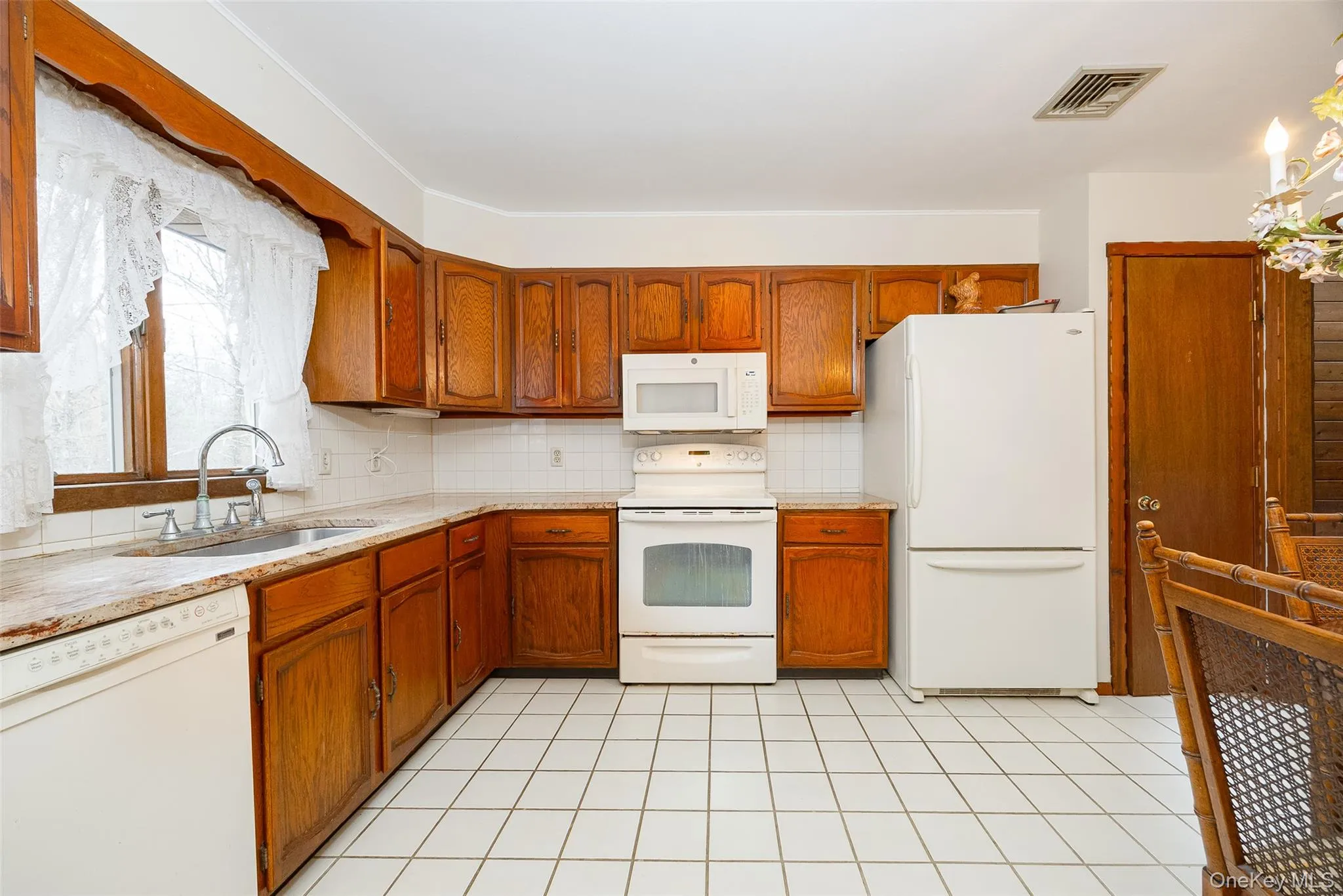 Kitchen with white appliances, tasteful backsplash, brown cabinets, and light tile patterned floors Kitchen with white appliances, tasteful backsplash, brown cabinets, and light tile patterned floors