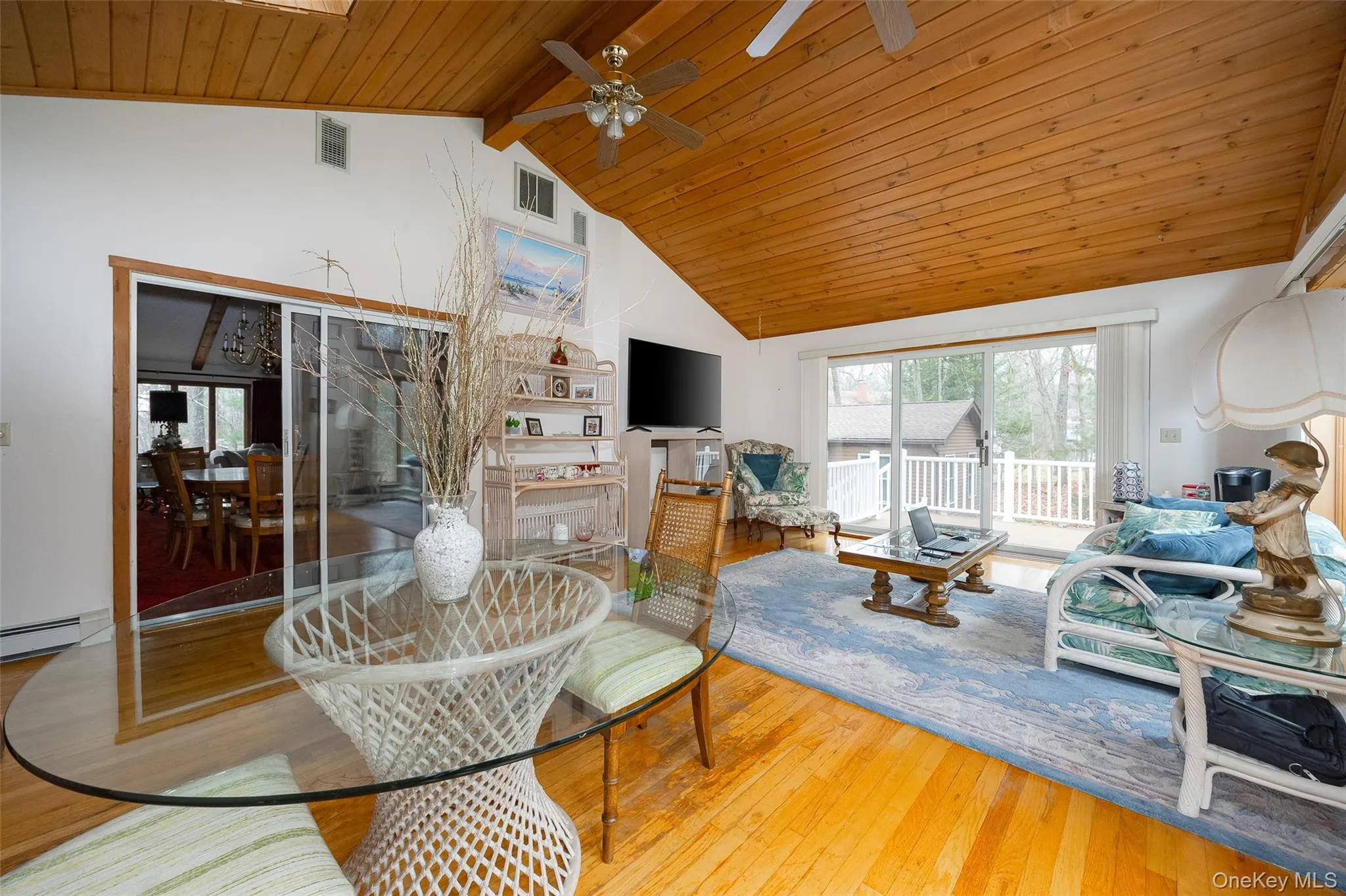 Living room with a wooden ceiling with exposed beams, light wood finished floors, ceiling fan, and high vaulted ceiling Living room with a wooden ceiling with exposed beams, light wood finished floors, ceiling fan, and high vaulted ceiling