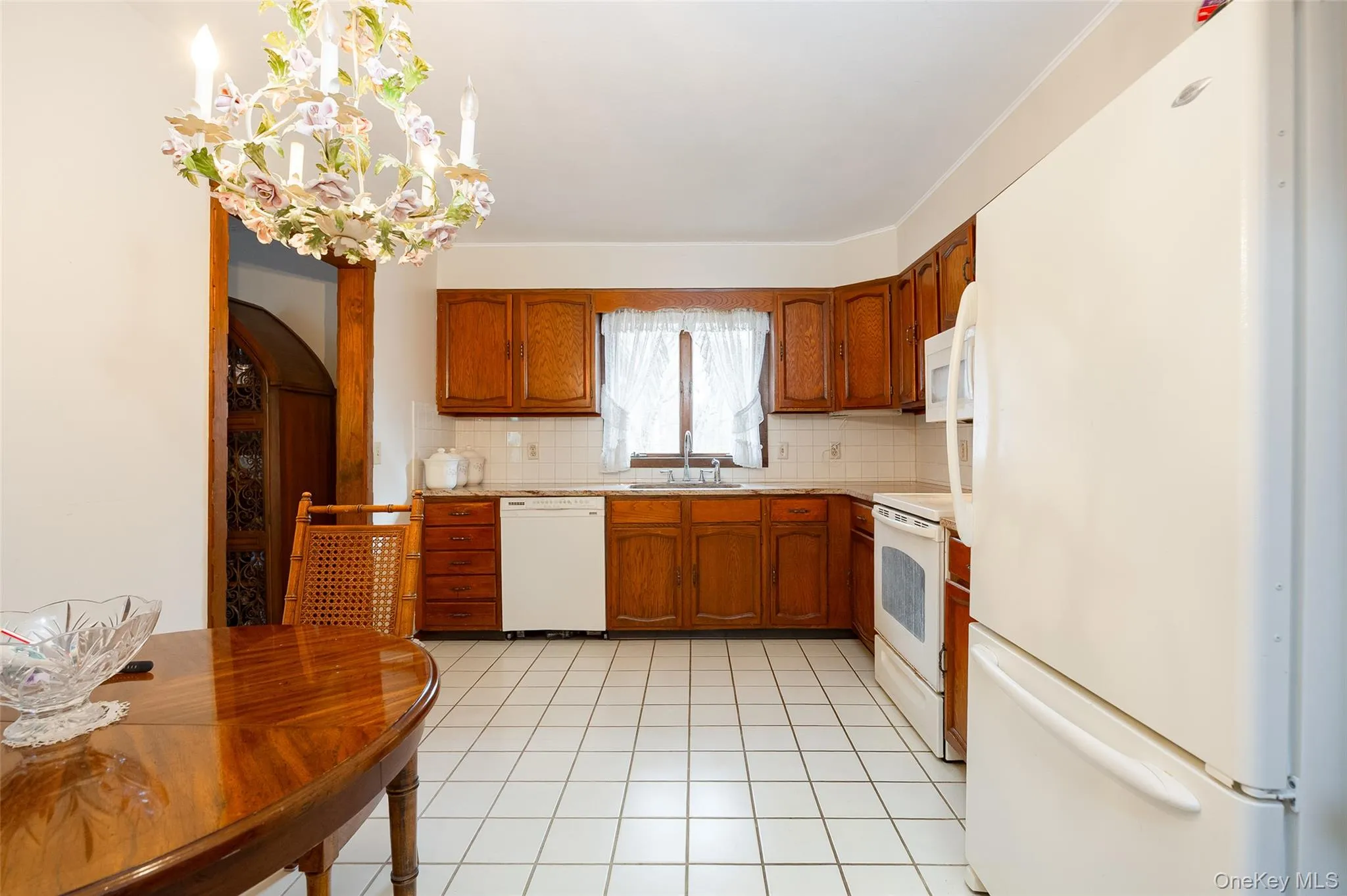 Kitchen featuring white appliances, light countertops, brown cabinets, decorative backsplash, and light tile patterned floors Kitchen featuring white appliances, light countertops, brown cabinets, decorative backsplash, and light tile patterned floors