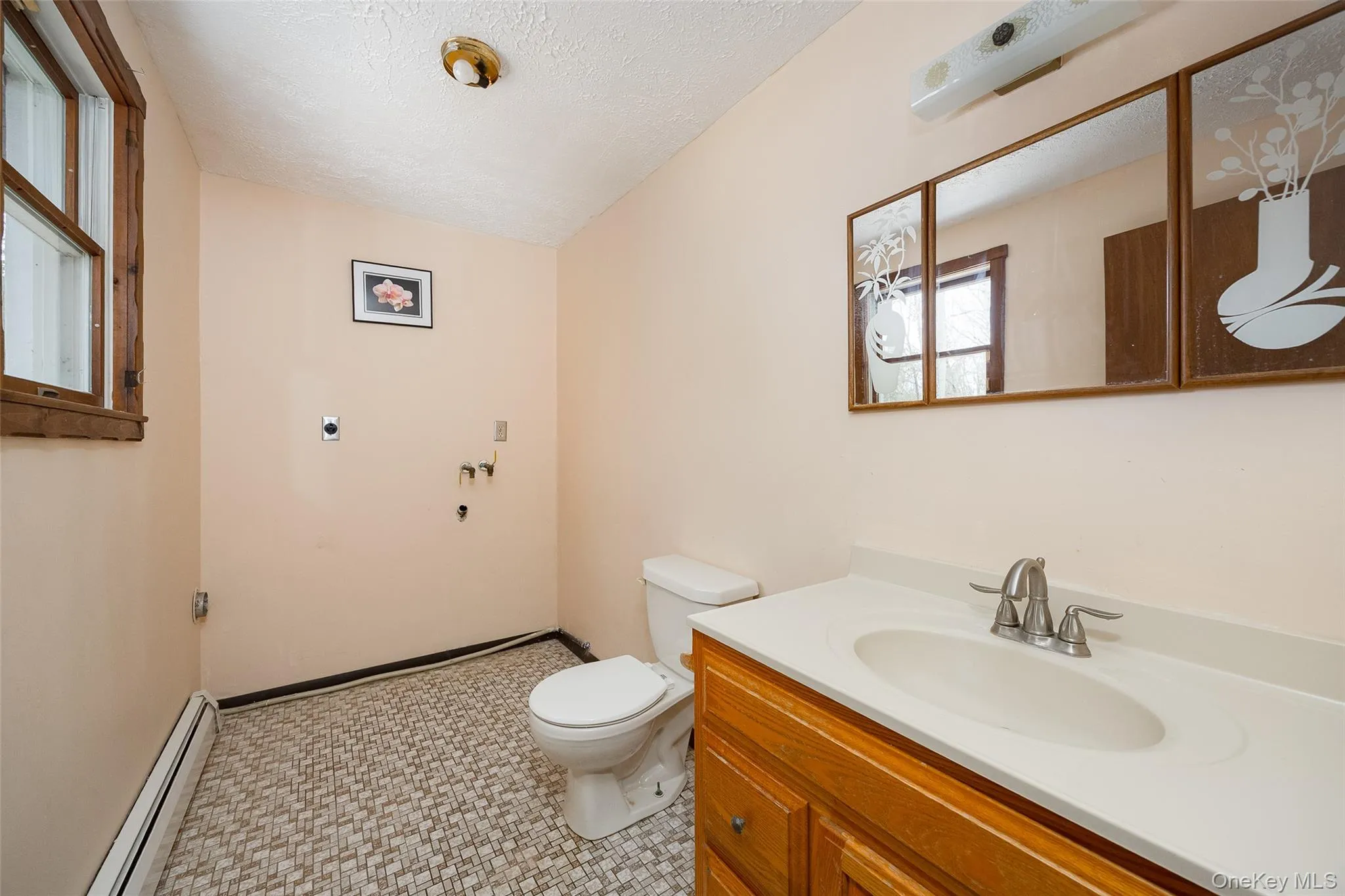 Half bathroom with a baseboard heating unit, vanity, a textured ceiling, and light flooring Half bathroom with a baseboard heating unit, vanity, a textured ceiling, and light flooring