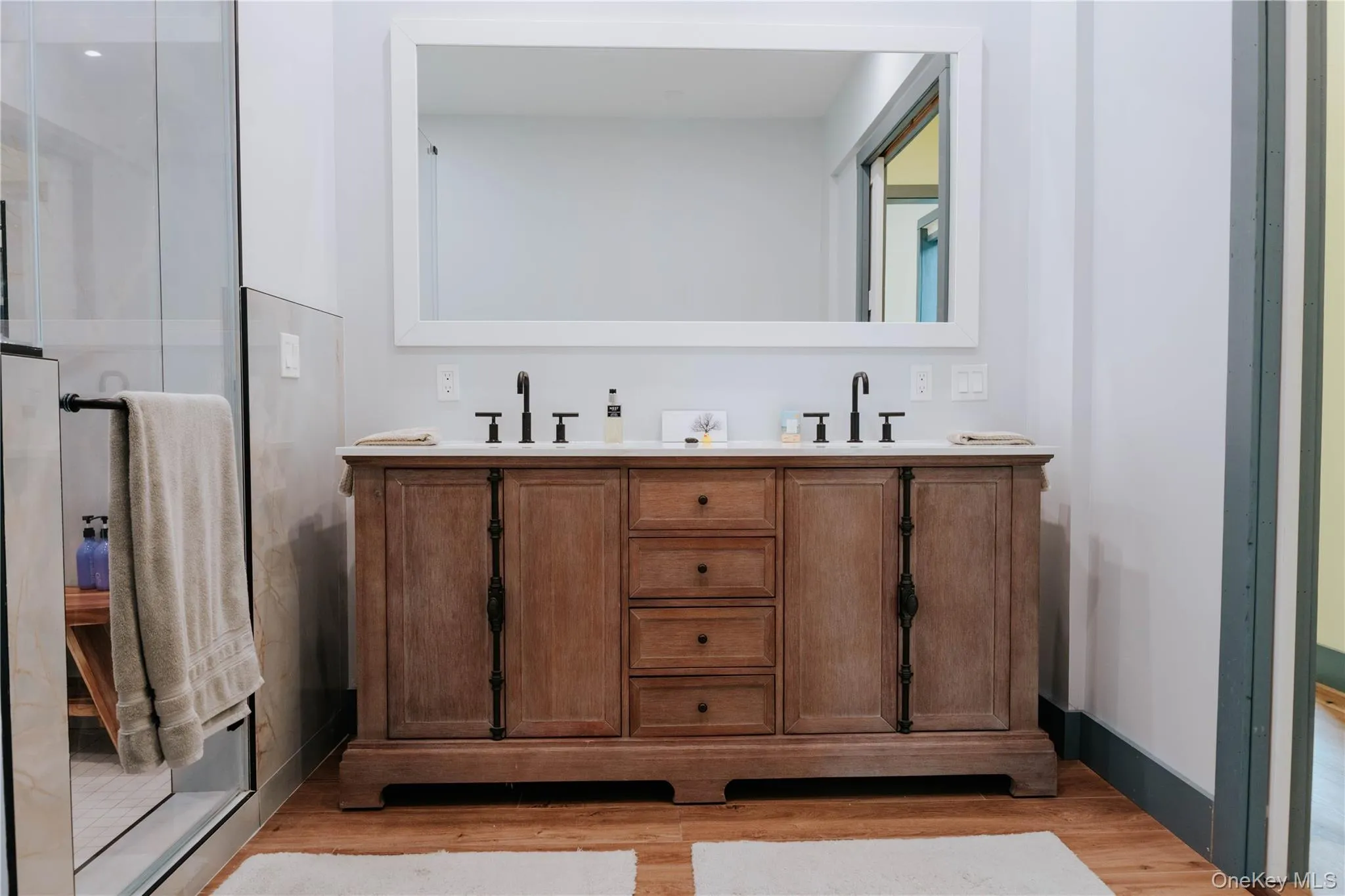 Bathroom featuring double vanity, wood finished floors, and an enclosed shower Bathroom featuring double vanity, wood finished floors, and an enclosed shower