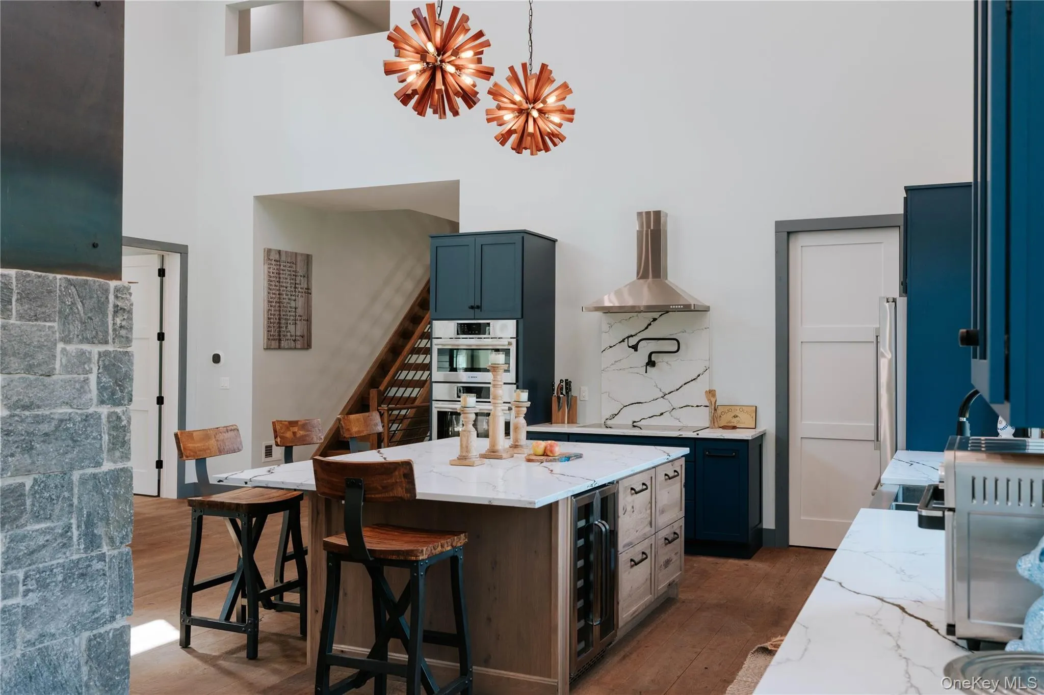 Kitchen featuring dark wood finished floors, light stone counters, wine cooler, wall chimney range hood, and a center island Kitchen featuring dark wood finished floors, light stone counters, wine cooler, wall chimney range hood, and a center island