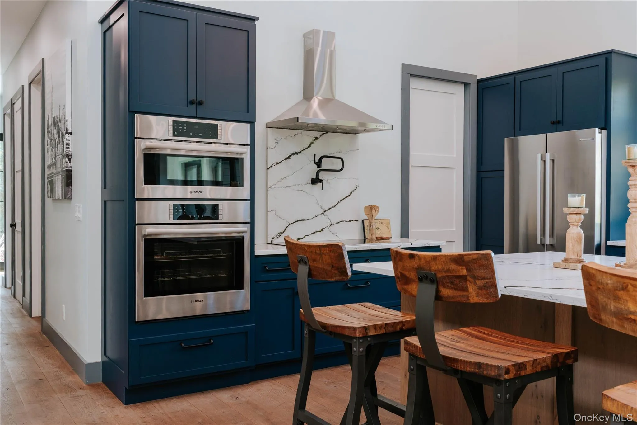 Kitchen featuring blue cabinetry, wall chimney exhaust hood, appliances with stainless steel finishes, and light wood-style floors Kitchen featuring blue cabinetry, wall chimney exhaust hood, appliances with stainless steel finishes, and light wood-style floors