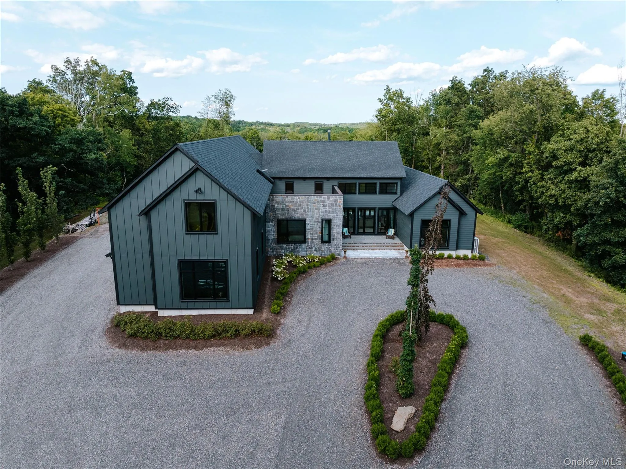 View of front of house with board and batten siding, curved driveway, stone siding, and a view of trees View of front of house with board and batten siding, curved driveway, stone siding, and a view of trees
