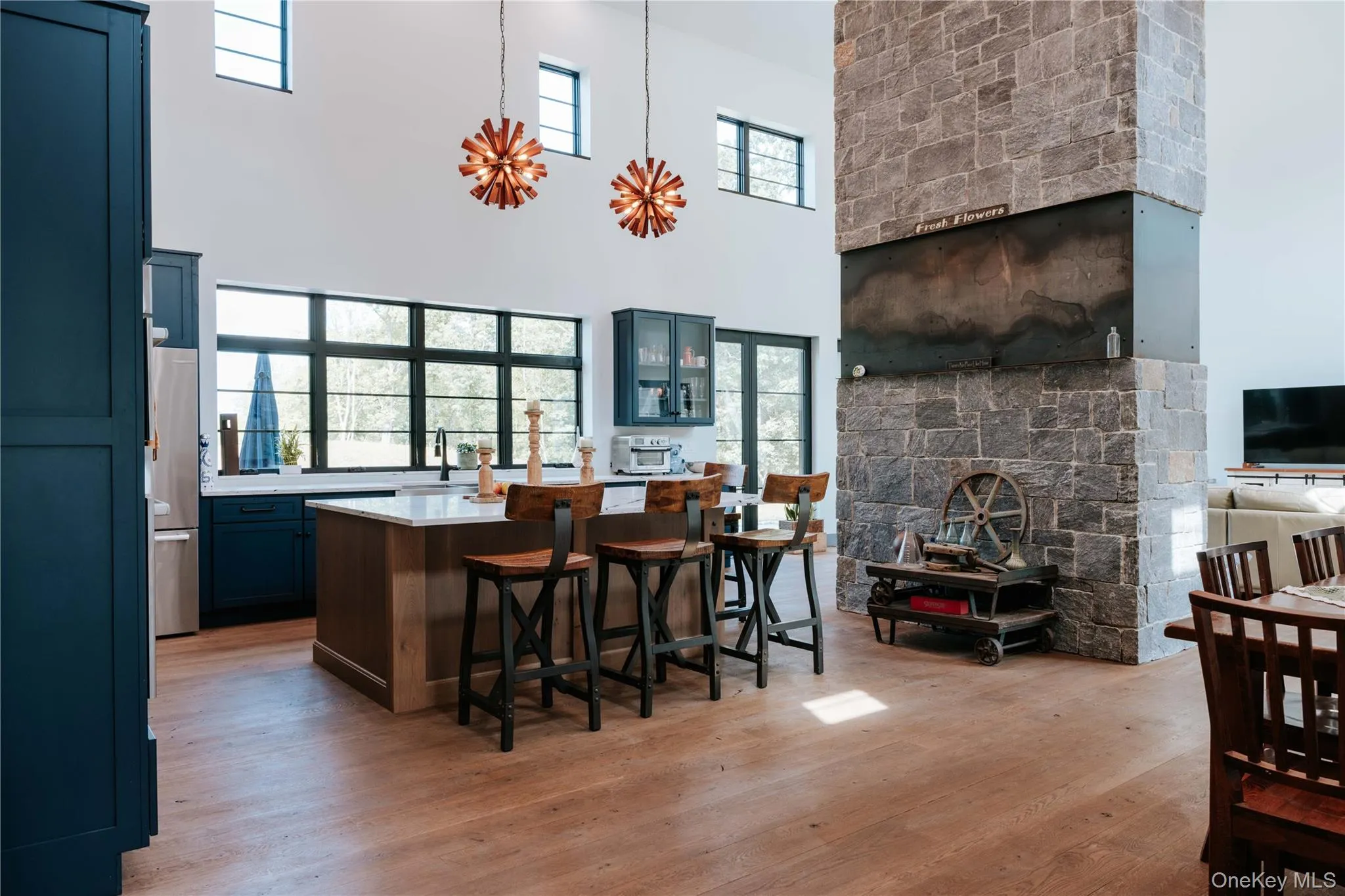 Bar with light wood-style floors, a high ceiling, pendant lighting, stainless steel fridge, and a fireplace Bar with light wood-style floors, a high ceiling, pendant lighting, stainless steel fridge, and a fireplace