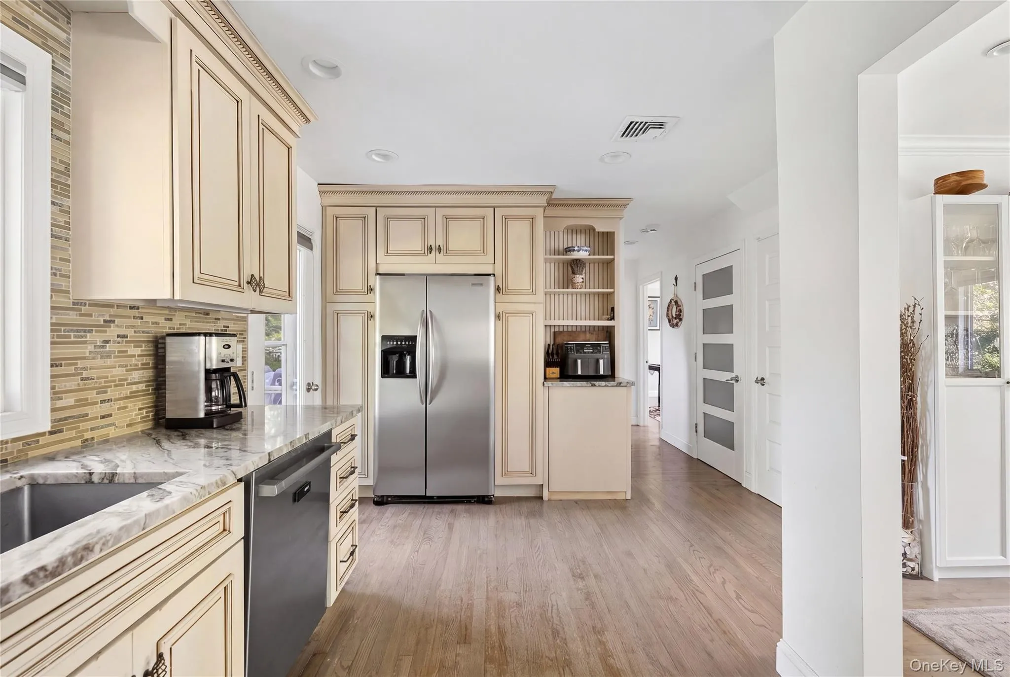 Kitchen featuring wood-finish flooring, stainless steel appliances, custom cabinetry, a tile backsplash, and stone countertops Kitchen featuring wood-finish flooring, stainless steel appliances, custom cabinetry, a tile backsplash, and stone countertops