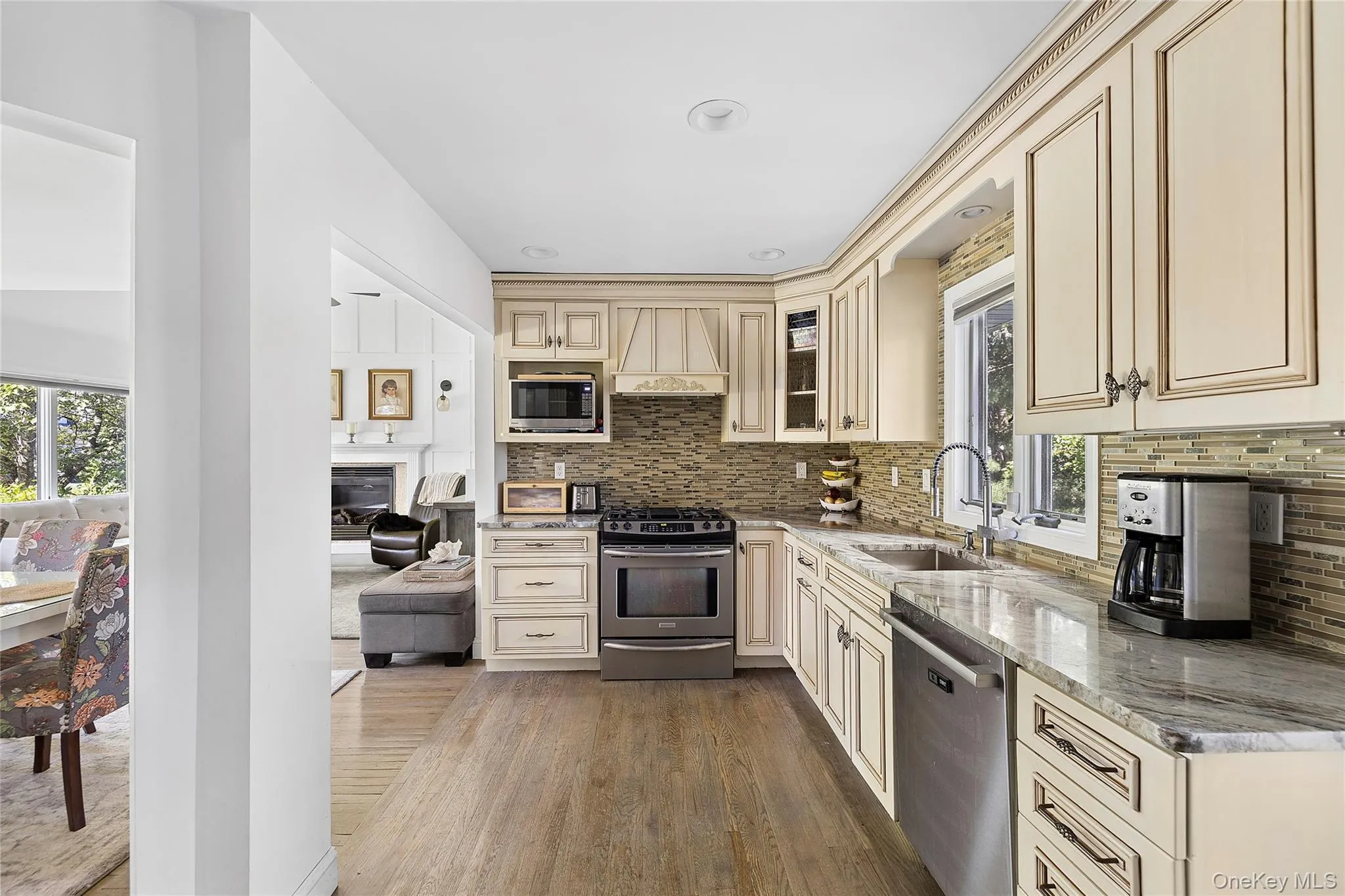 Kitchen featuring wood-finish flooring, cream cabinetry, a tile backsplash, and stone countertops Kitchen featuring wood-finish flooring, cream cabinetry, a tile backsplash, and stone countertops
