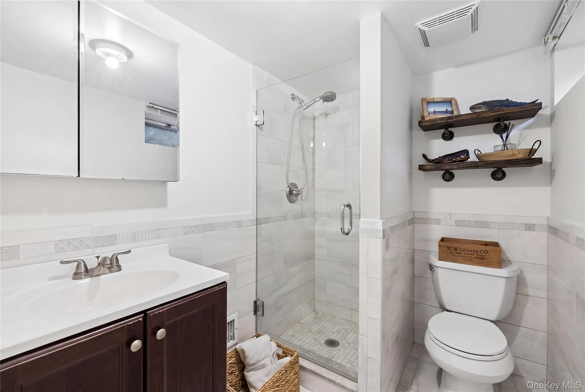 Contemporary bathroom featuring a glass-enclosed shower with tile surround, a dark wood-finish vanity with an integrated sink, brushed nickel faucet, and a wall-mounted mirrored medicine cabinet Contemporary bathroom featuring a glass-enclosed shower with tile surround, a dark wood-finish vanity with an integrated sink, brushed nickel faucet, and a wall-mounted mirrored medicine cabinet