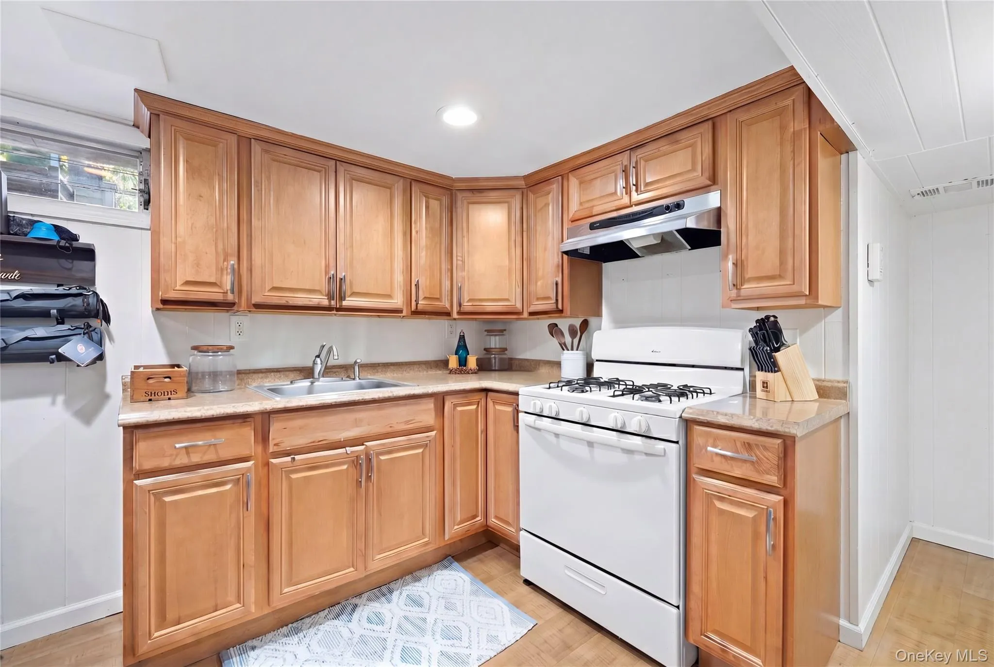 Corner kitchen featuring wood-finish cabinetry, light-toned countertops, and a white gas range with an overhead exhaust fan Corner kitchen featuring wood-finish cabinetry, light-toned countertops, and a white gas range with an overhead exhaust fan