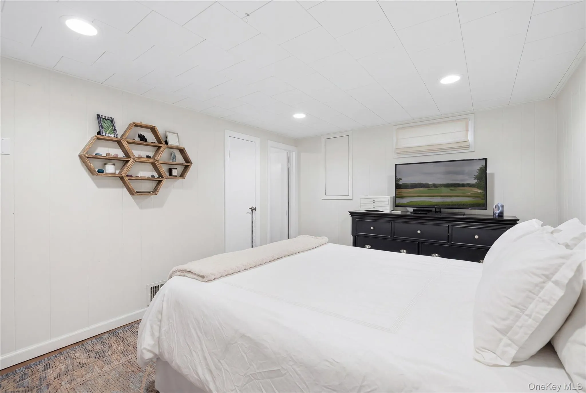 Recessed lighting illuminates this space featuring light-colored wall paneling, a window with a roman shade, and wood-finish flooring Recessed lighting illuminates this space featuring light-colored wall paneling, a window with a roman shade, and wood-finish flooring