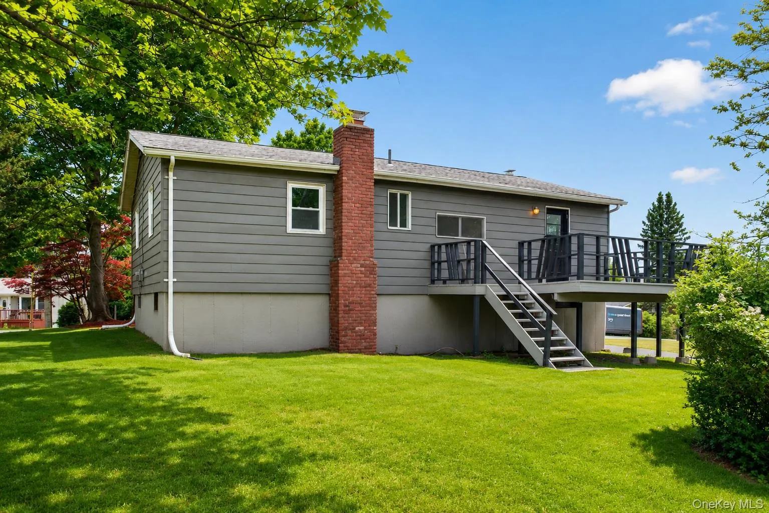 Rear exterior with grey siding, a red brick chimney, and a multi-level deck with black railings Rear exterior with grey siding, a red brick chimney, and a multi-level deck with black railings