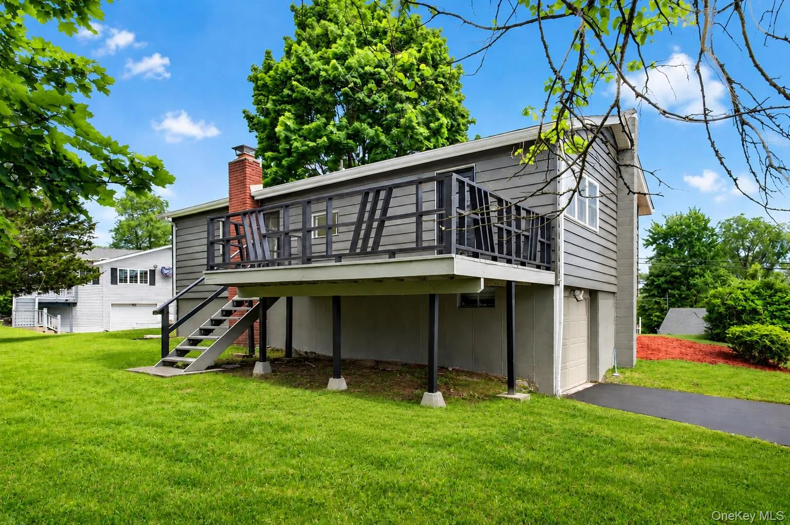 Raised deck with dark railings, gray siding, a prominent brick chimney, and a lower-level garage access Raised deck with dark railings, gray siding, a prominent brick chimney, and a lower-level garage access