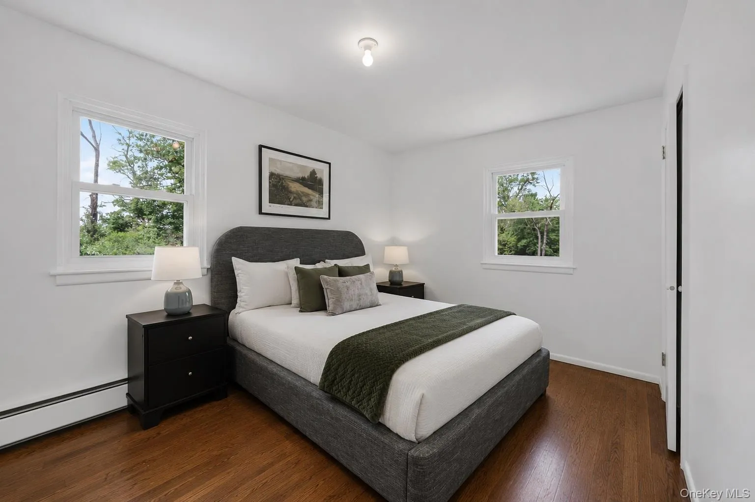 Bedroom featuring two windows with white trim, wood-finish flooring, and white walls Bedroom featuring two windows with white trim, wood-finish flooring, and white walls