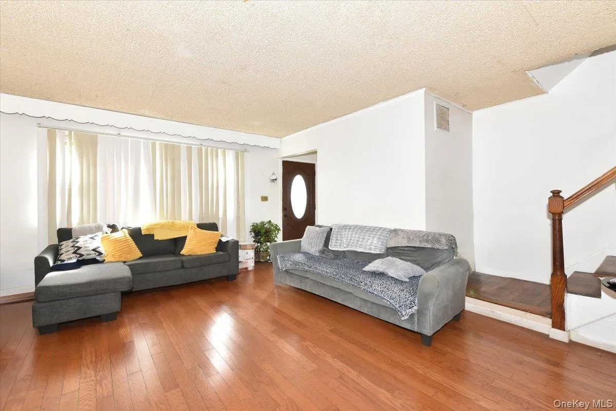 Living room with hardwood / wood-style flooring, visible vents, stairway, and a textured ceiling Living room with hardwood / wood-style flooring, visible vents, stairway, and a textured ceiling