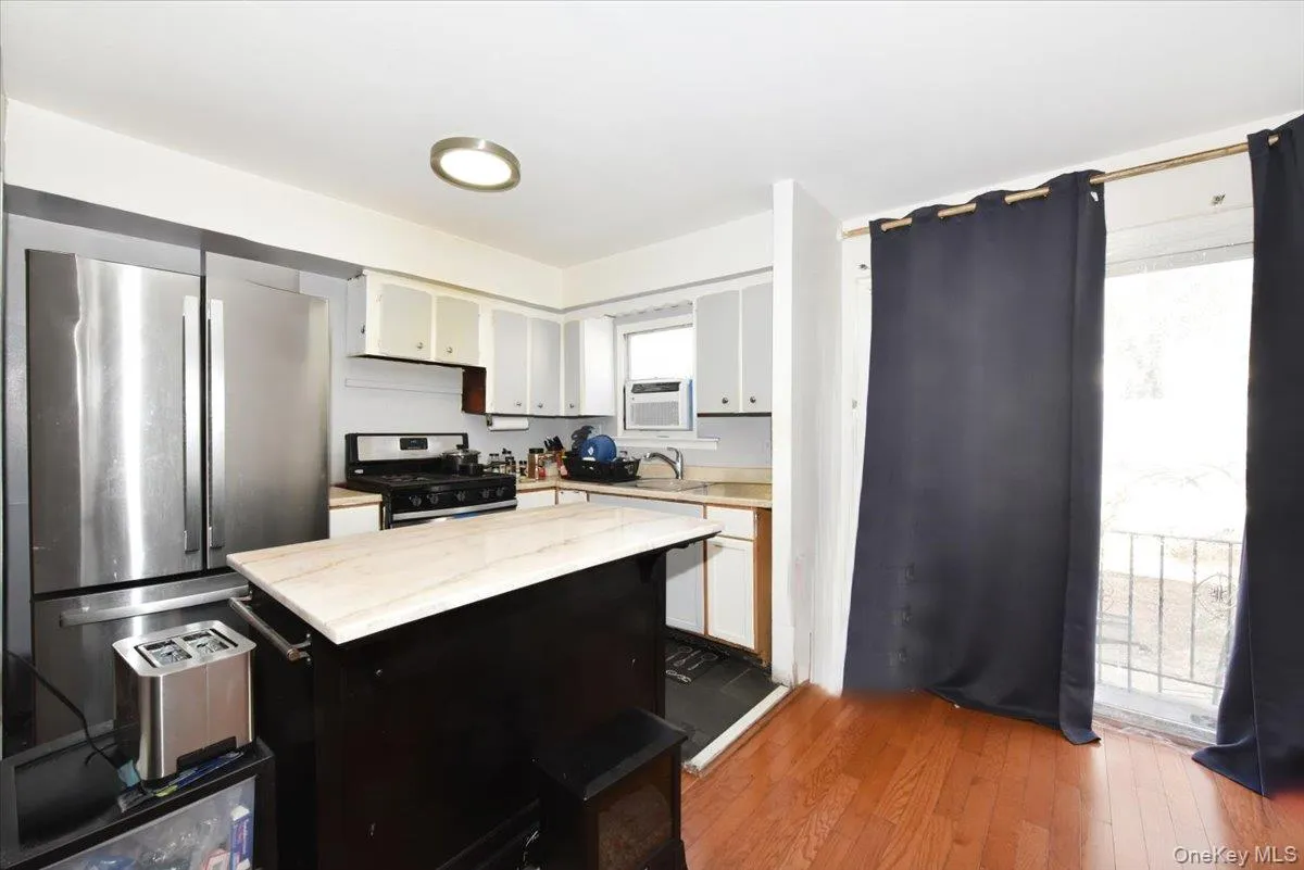 Kitchen featuring white cabinets, wood finished floors, light stone countertops, stainless steel appliances, and a sink Kitchen featuring white cabinets, wood finished floors, light stone countertops, stainless steel appliances, and a sink