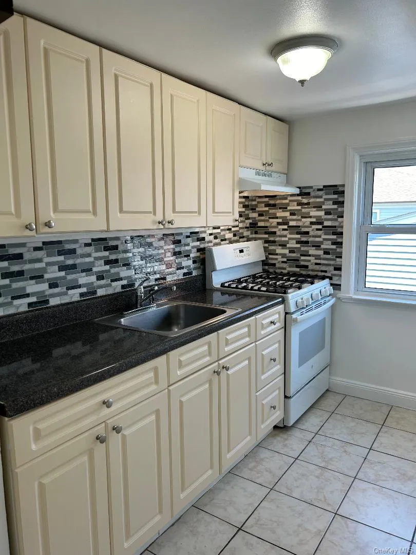 Kitchen featuring a sink, backsplash, white range with gas cooktop, under cabinet range hood, and light tile patterned floors Kitchen featuring a sink, backsplash, white range with gas cooktop, under cabinet range hood, and light tile patterned floors