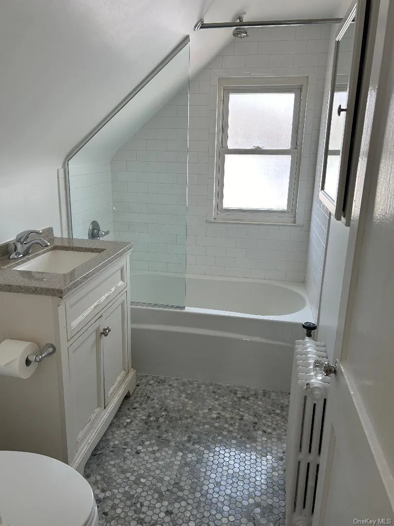 Bathroom with radiator heating unit, tile patterned flooring, toilet, vanity, and tub / shower combination Bathroom with radiator heating unit, tile patterned flooring, toilet, vanity, and tub / shower combination