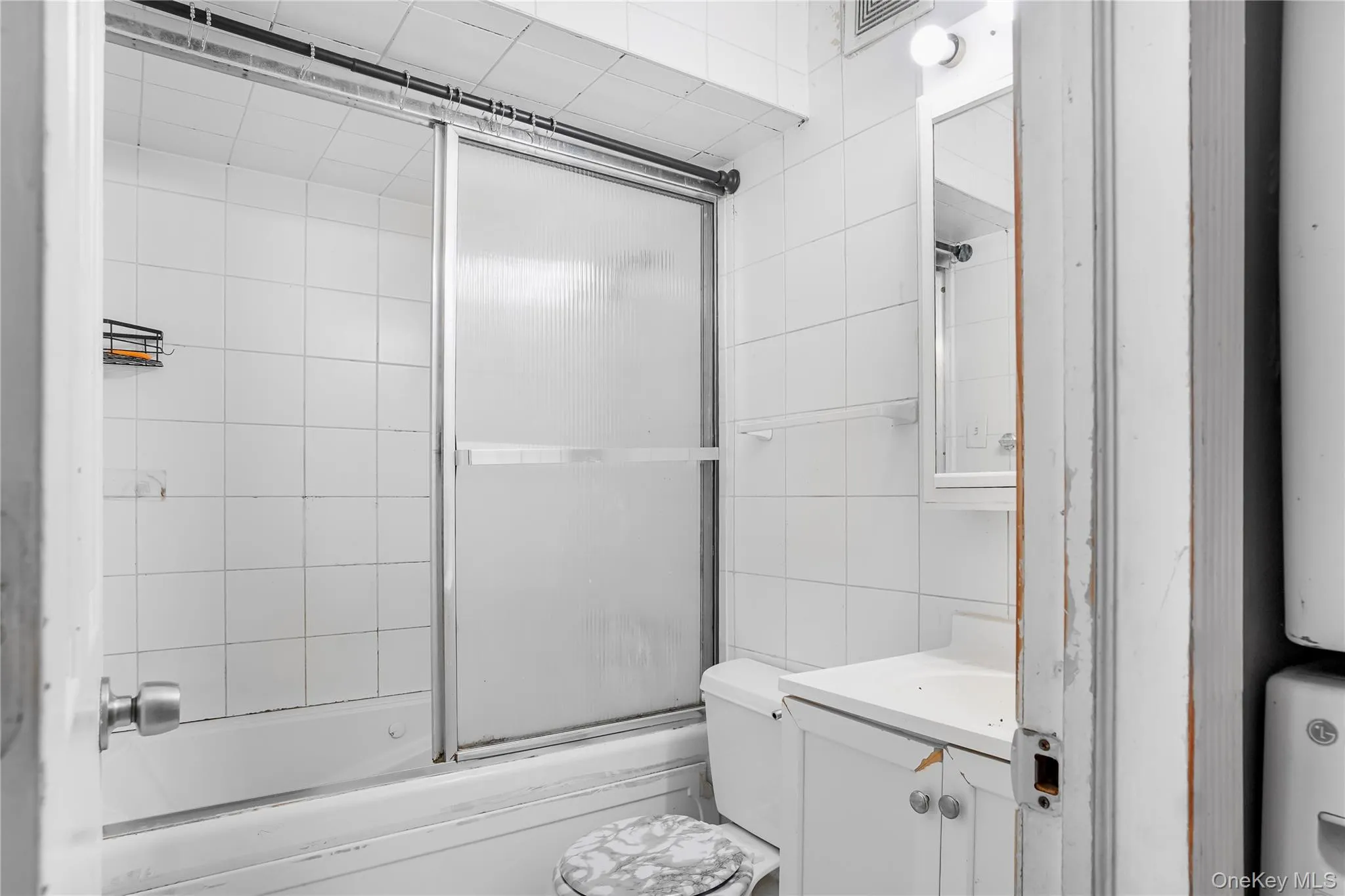 Full bathroom featuring a white tile shower surround with sliding glass doors, a white bathtub, and a vanity with a white countertop and base cabinetry Full bathroom featuring a white tile shower surround with sliding glass doors, a white bathtub, and a vanity with a white countertop and base cabinetry