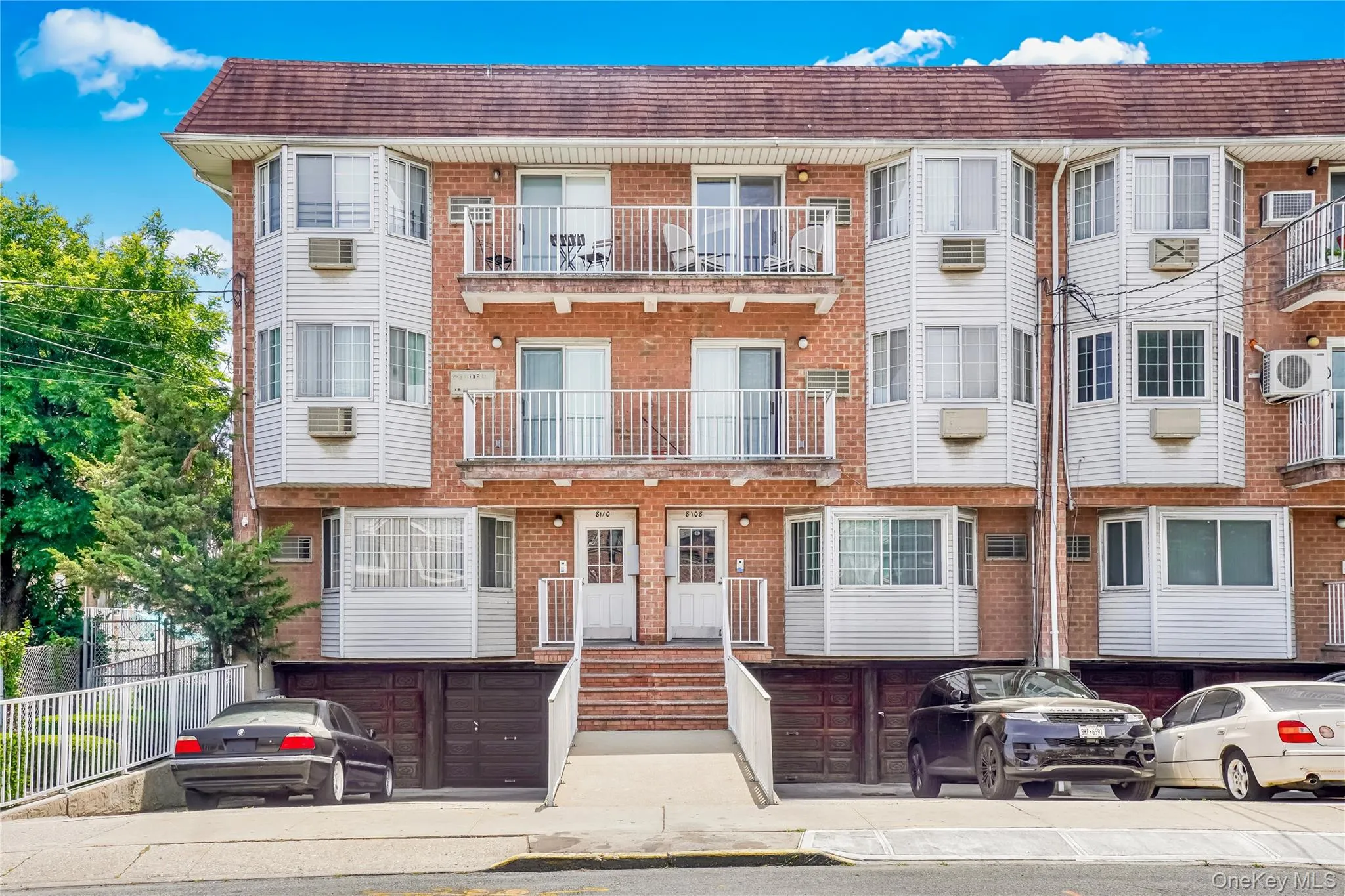Multi-unit brick building featuring white vinyl siding and multiple balconies with white railings Multi-unit brick building featuring white vinyl siding and multiple balconies with white railings