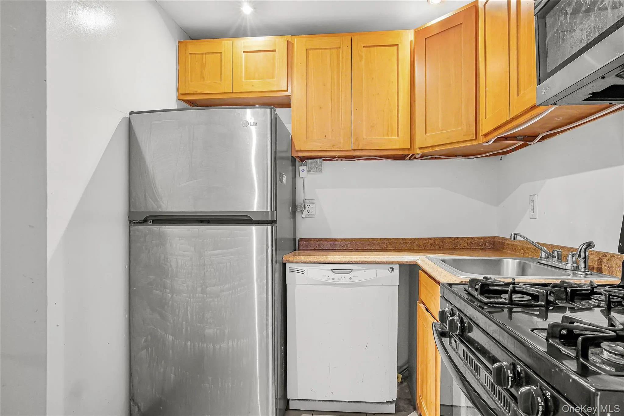 Compact kitchen featuring a stainless steel refrigerator, wood-finish cabinetry, a stainless steel sink, and a black gas range Compact kitchen featuring a stainless steel refrigerator, wood-finish cabinetry, a stainless steel sink, and a black gas range