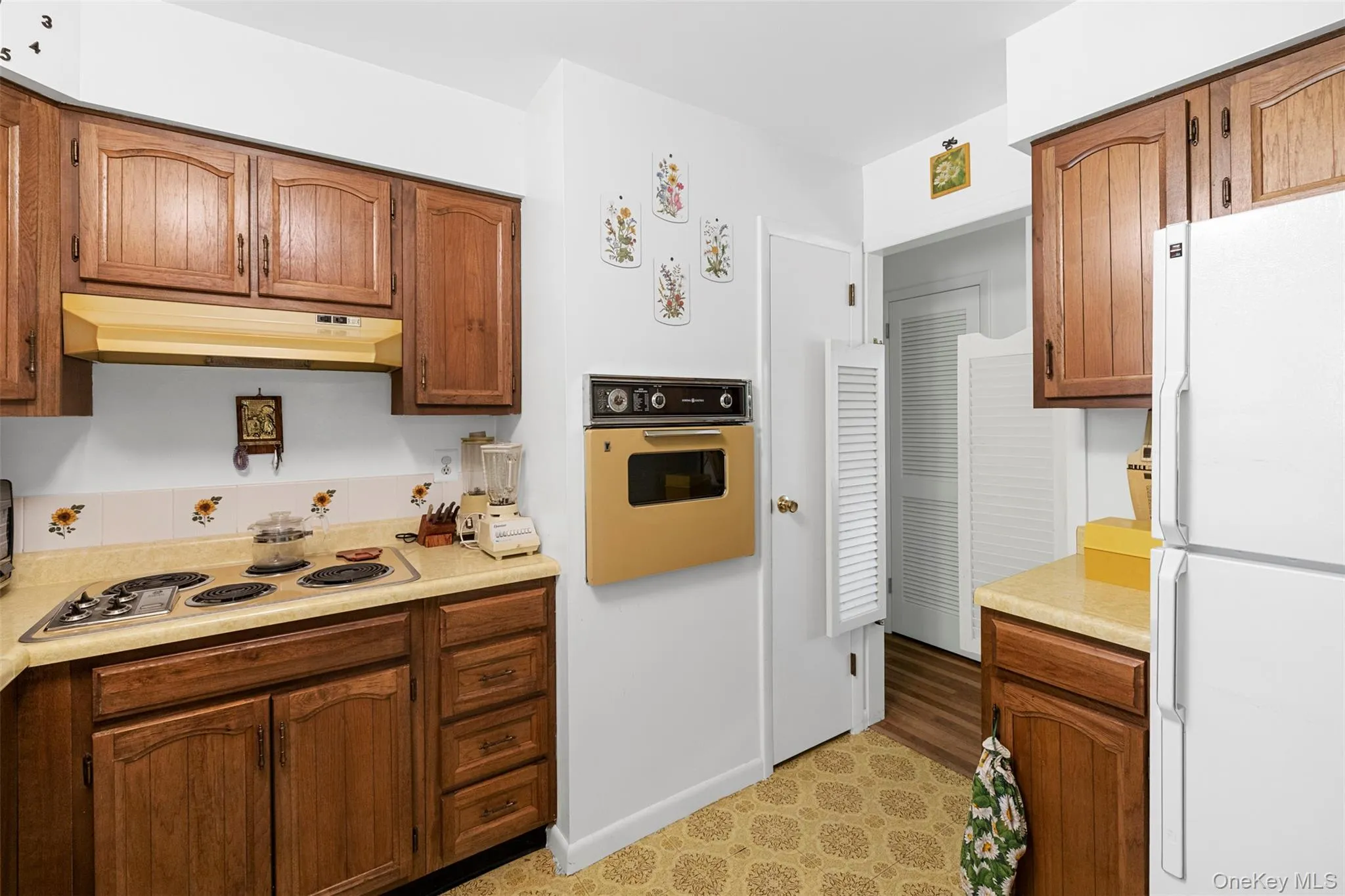 Kitchen with freestanding refrigerator, oven, electric stovetop, under cabinet range hood, and light countertops Kitchen with freestanding refrigerator, oven, electric stovetop, under cabinet range hood, and light countertops