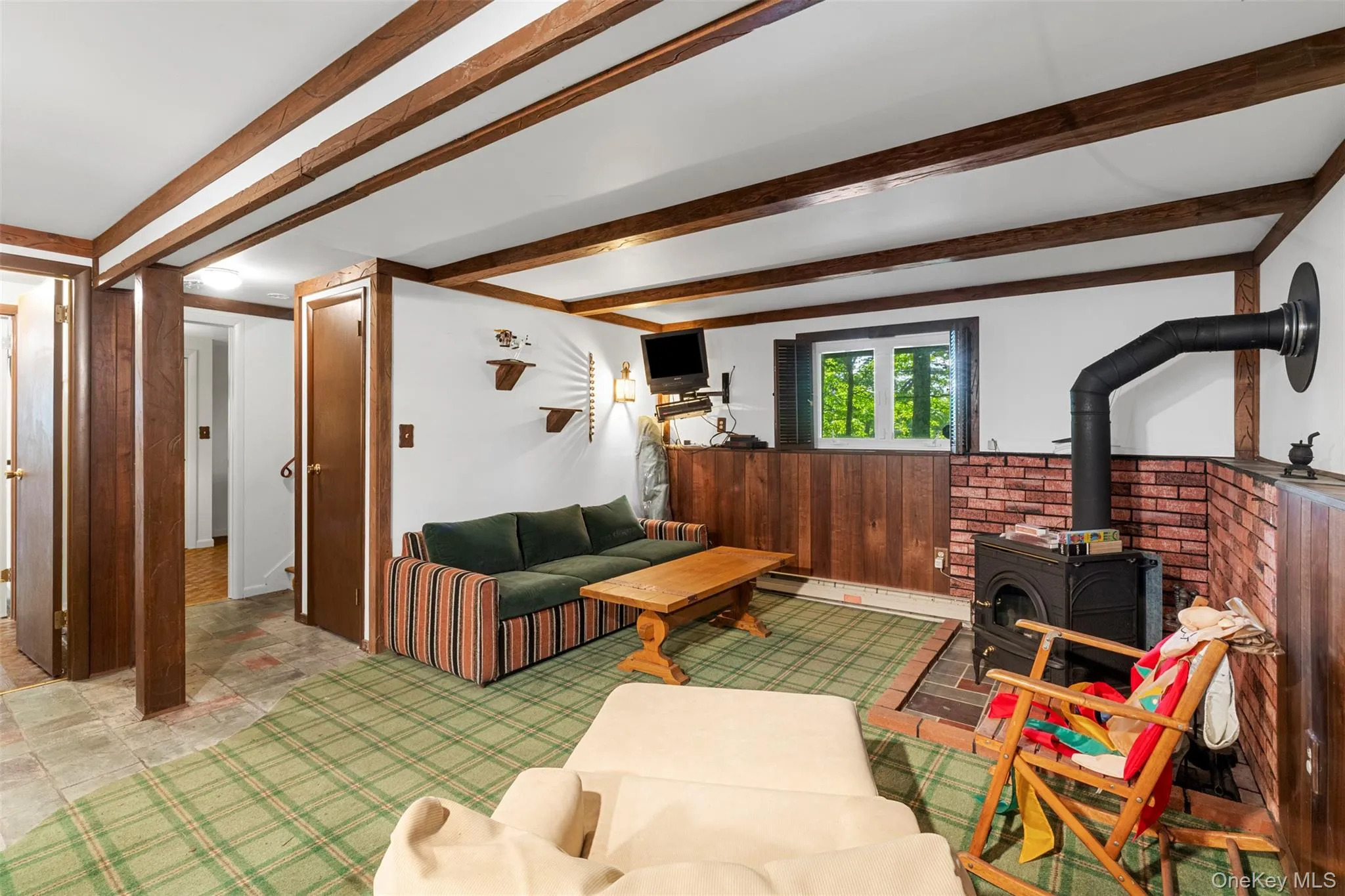 Living room featuring a wood stove, beam ceiling, wooden walls, and wainscoting Living room featuring a wood stove, beam ceiling, wooden walls, and wainscoting