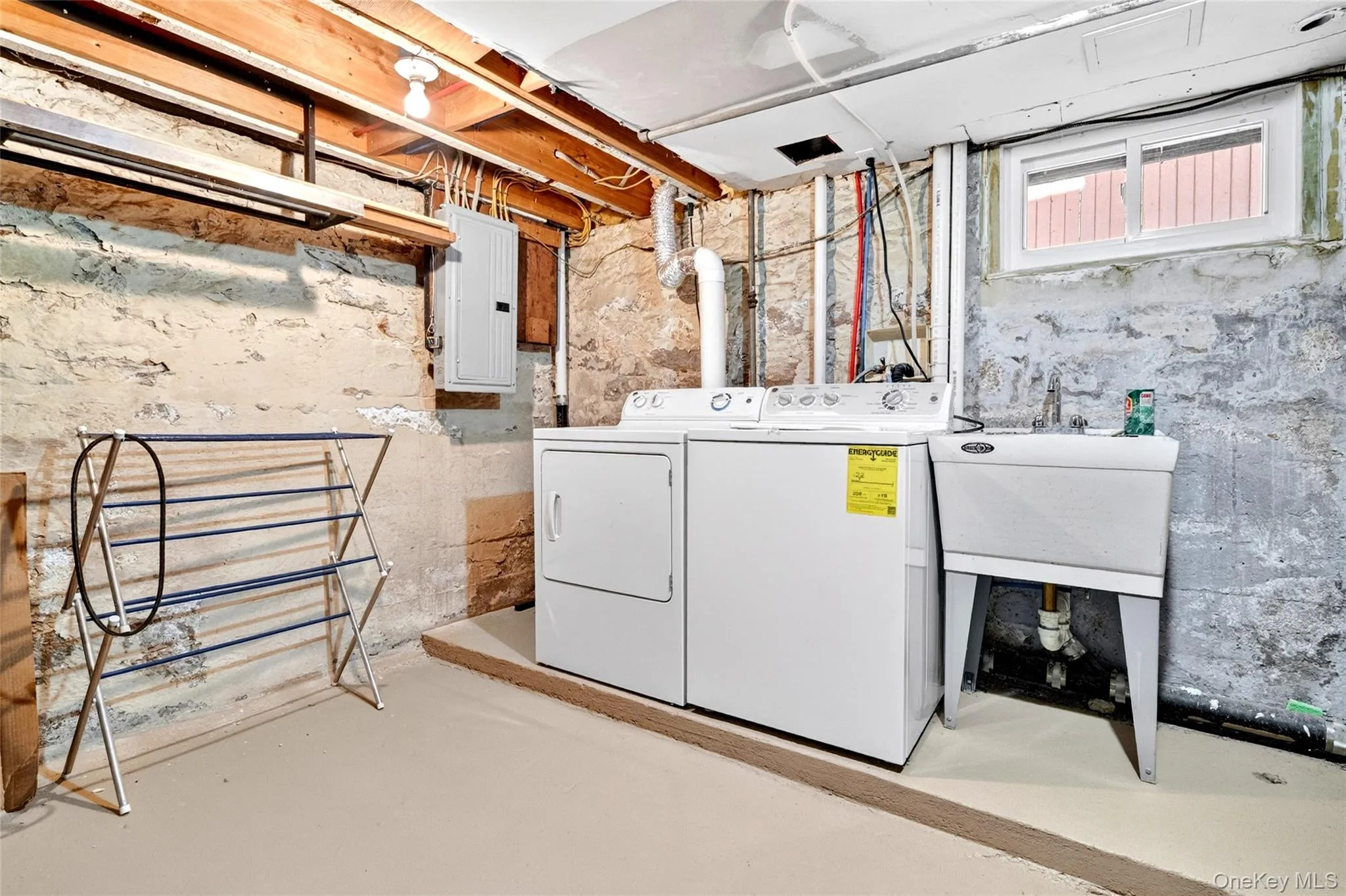 Laundry area featuring a utility sink, exposed ceiling joists, and concrete walls Laundry area featuring a utility sink, exposed ceiling joists, and concrete walls