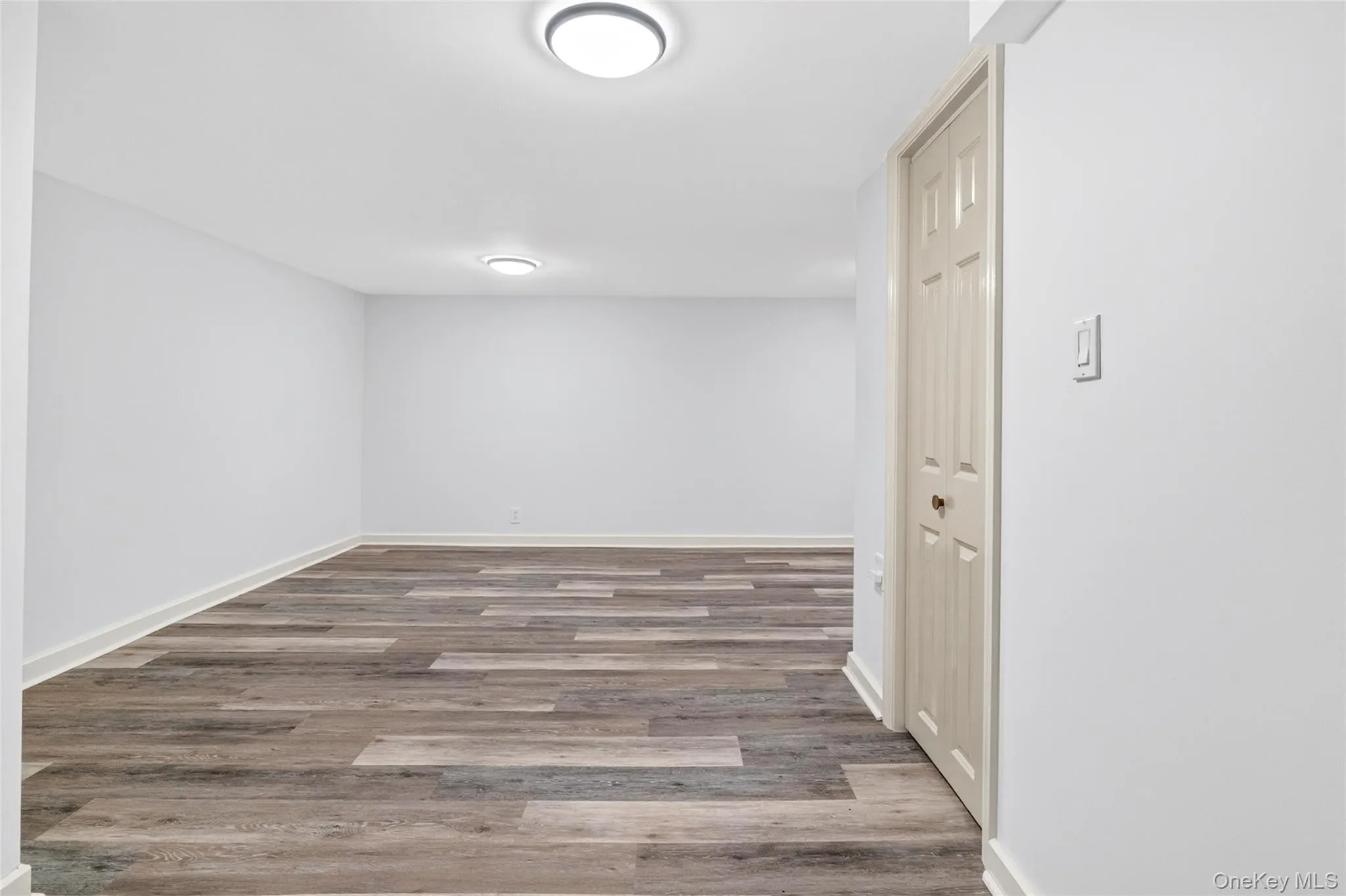 Spacious room featuring wood-finish flooring, white walls, and contemporary flush-mount lighting fixtures Spacious room featuring wood-finish flooring, white walls, and contemporary flush-mount lighting fixtures