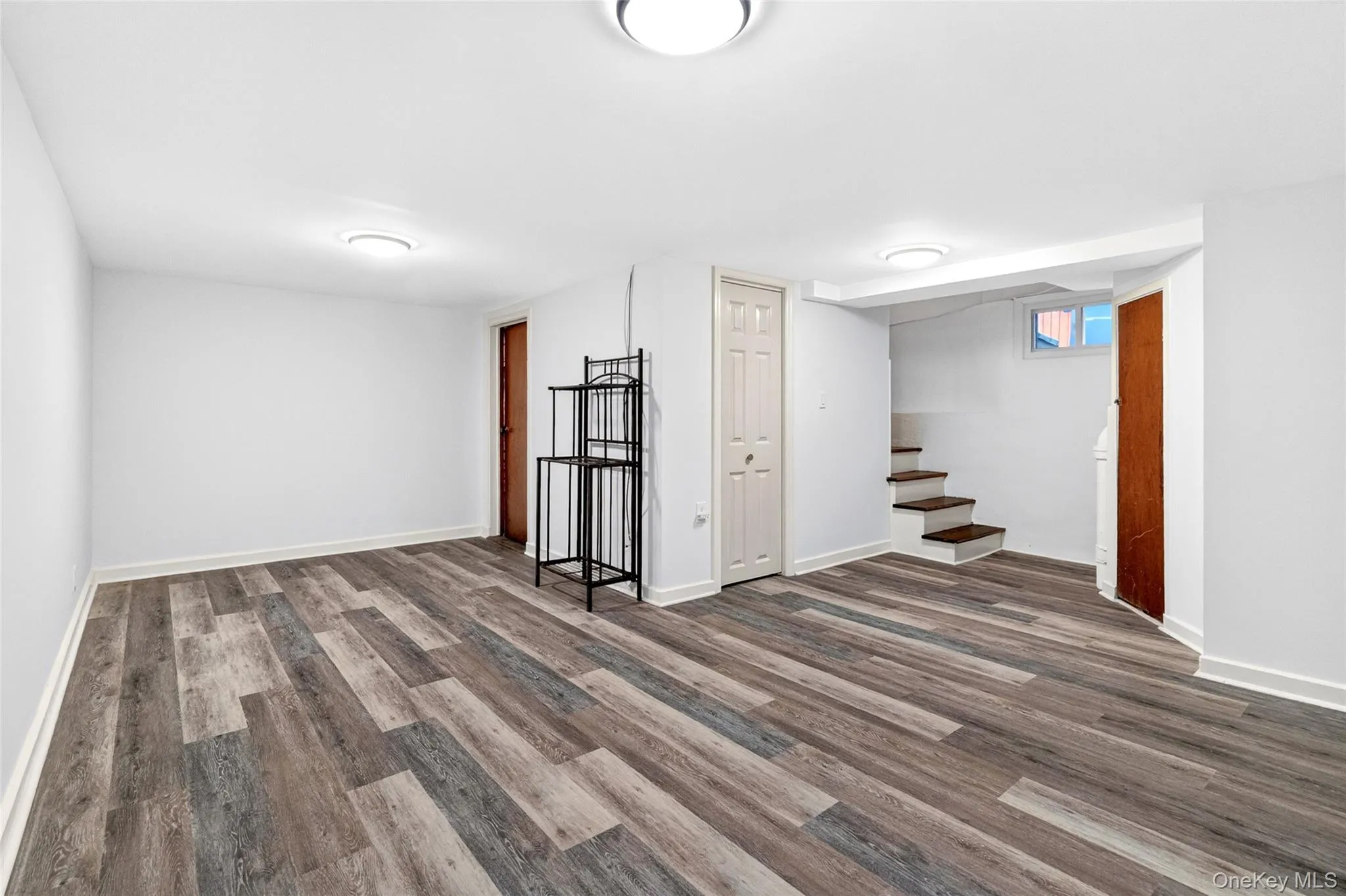 Spacious room with wood-finish flooring, white walls, and bright ceiling lighting Spacious room with wood-finish flooring, white walls, and bright ceiling lighting
