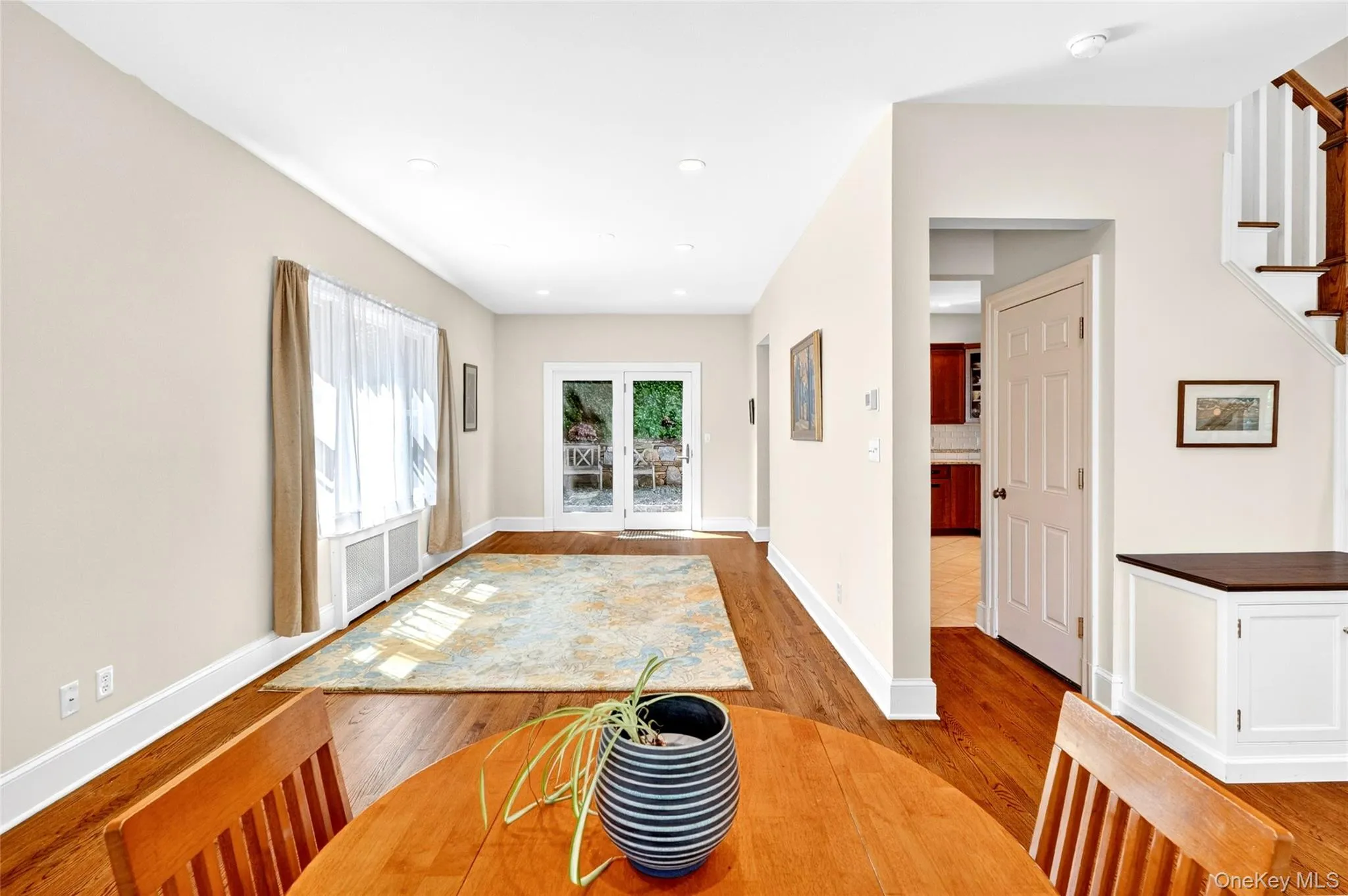 Hardwood flooring throughout a bright room featuring white trim, a large window with sheer and opaque drapes, and double French doors opening to an exterior Hardwood flooring throughout a bright room featuring white trim, a large window with sheer and opaque drapes, and double French doors opening to an exterior